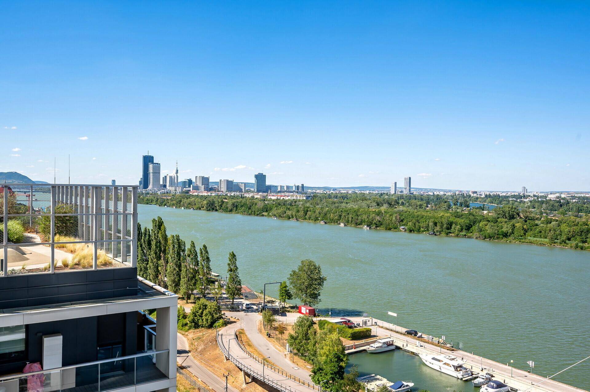 Panoramablick auf den Fluss, die Stadtlandschaft und die umliegende grüne Natur unter blauem Himmel.