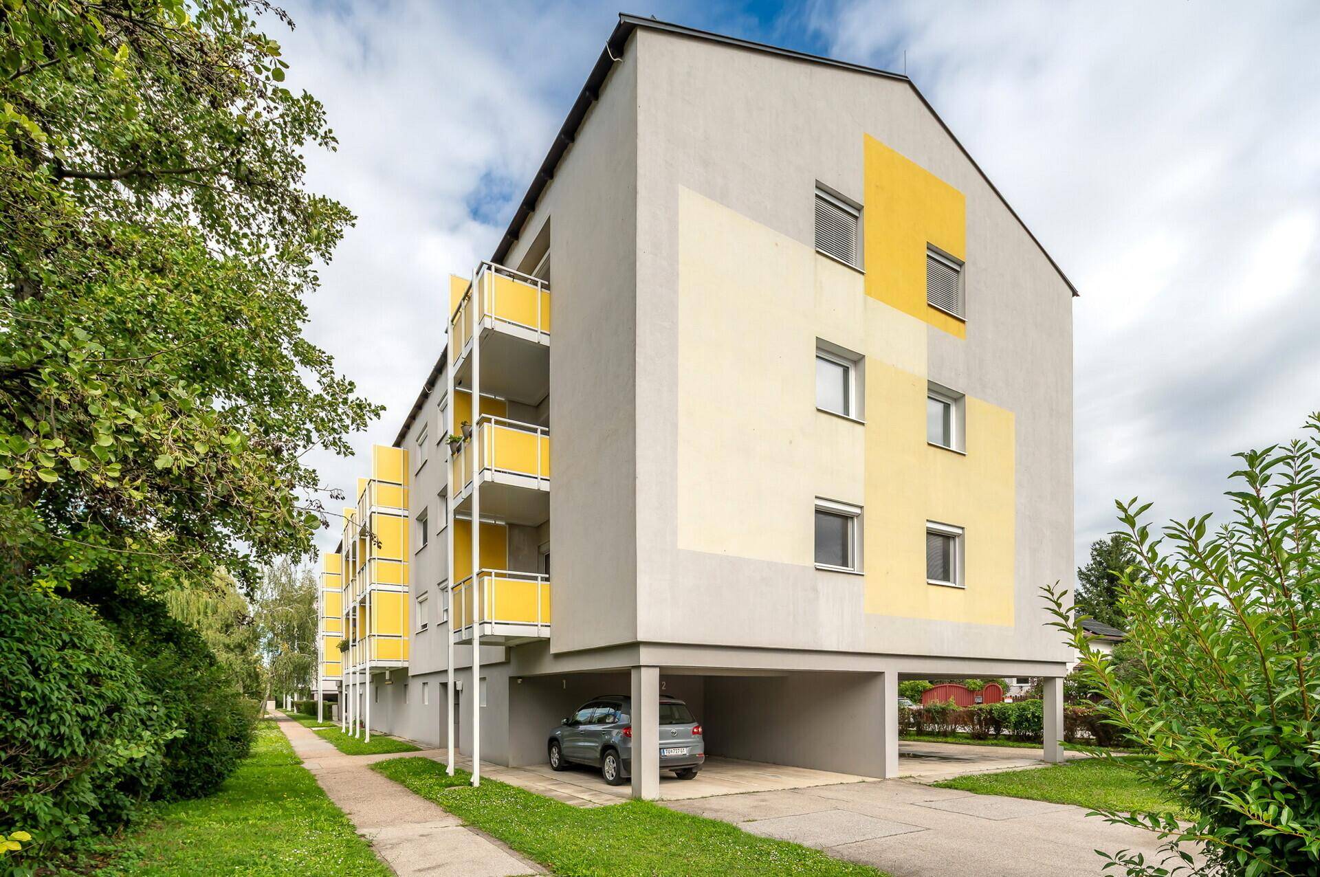 Modernes Mehrfamilienhaus mit gelben Akzenten, Balkonen und integrierten Carports.