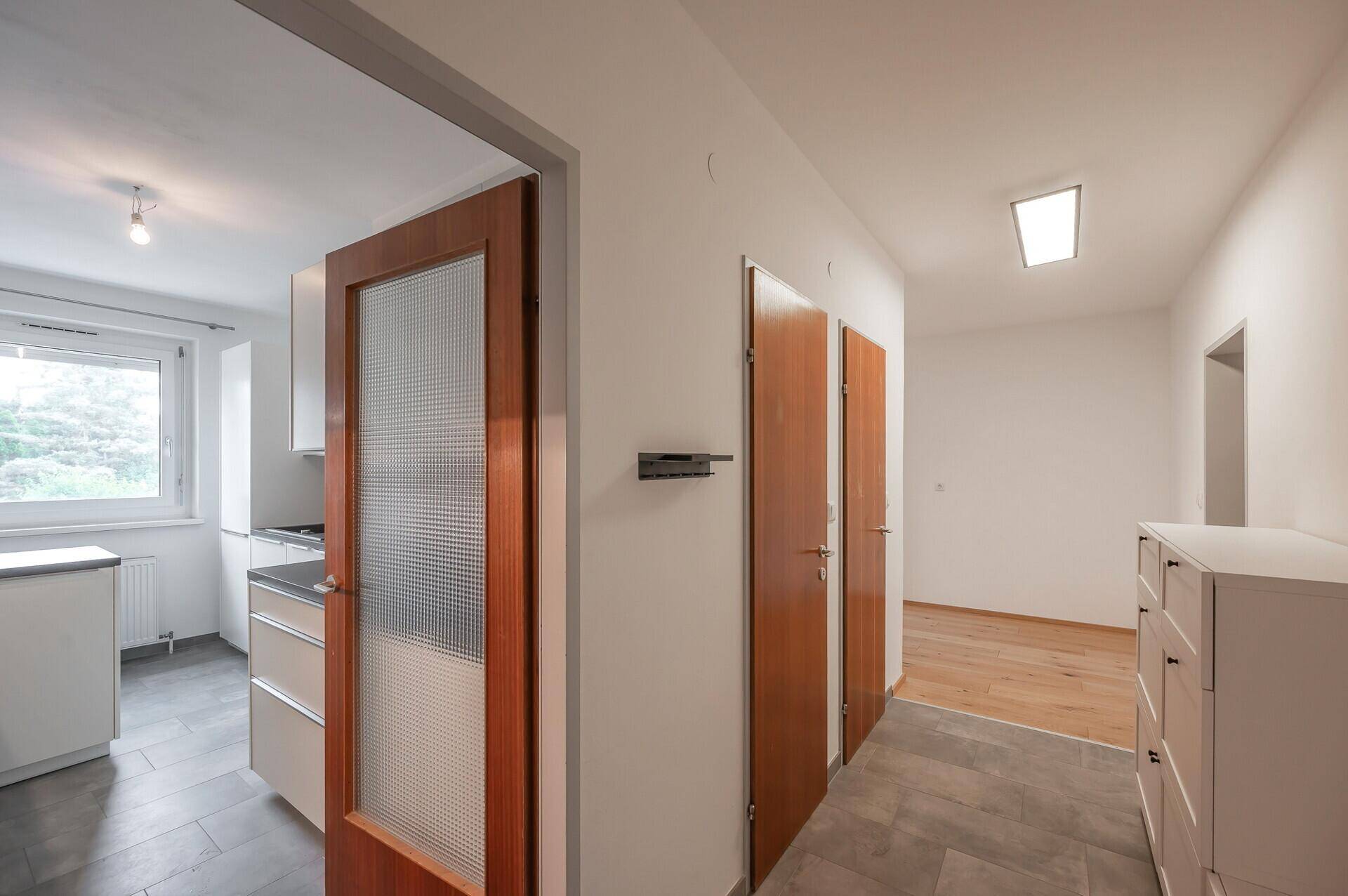 Heller Flur mit Fliesenboden, Holztüren und Blick in die angrenzende Küche.