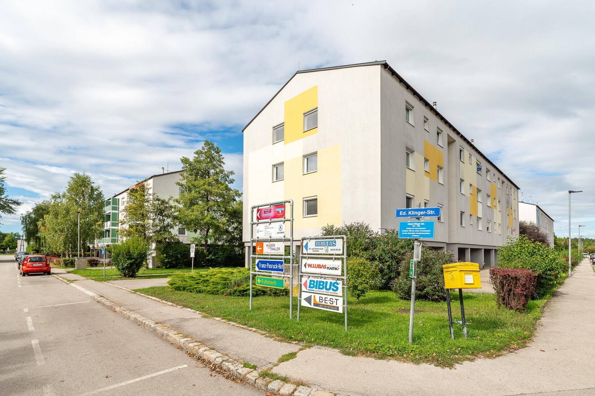 Straßenansicht mit Wohngebäuden, Informationsschildern und einem Briefkasten.