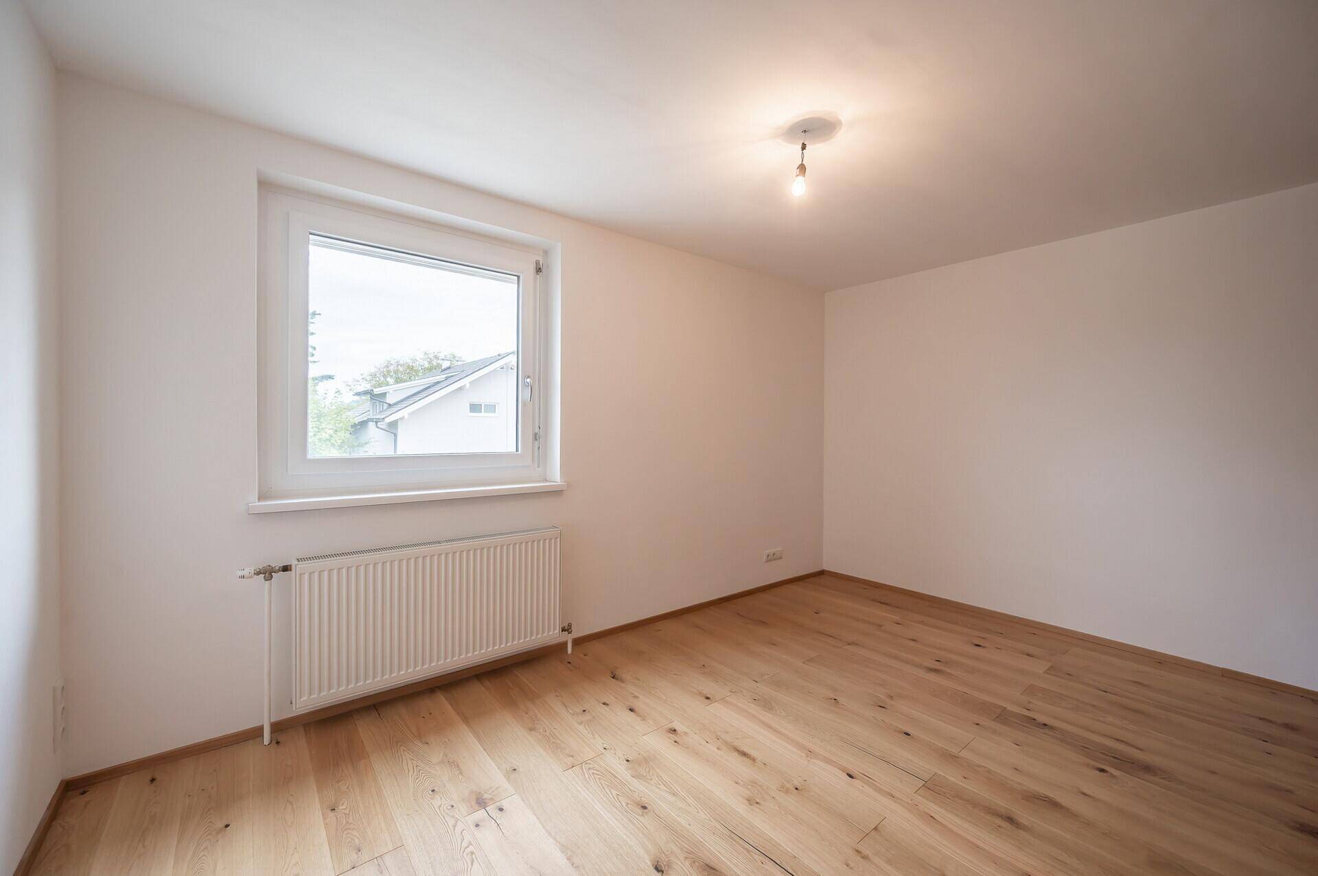 Helles Zimmer mit Parkettboden, weißen Wänden und großem Fenster.