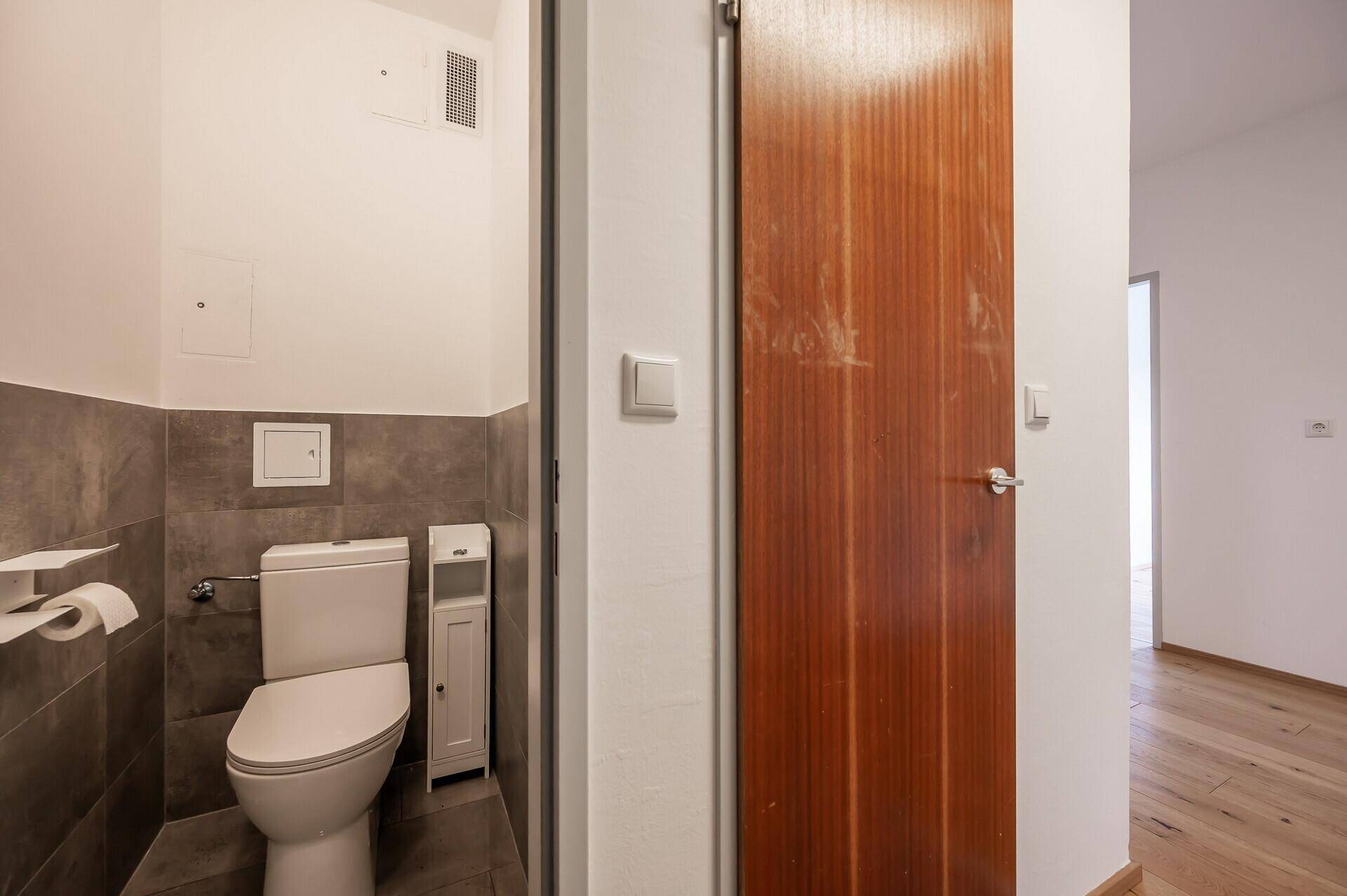 Kleines Gäste-WC mit Toilette, halbhohen Fliesen und Abluftsystem.