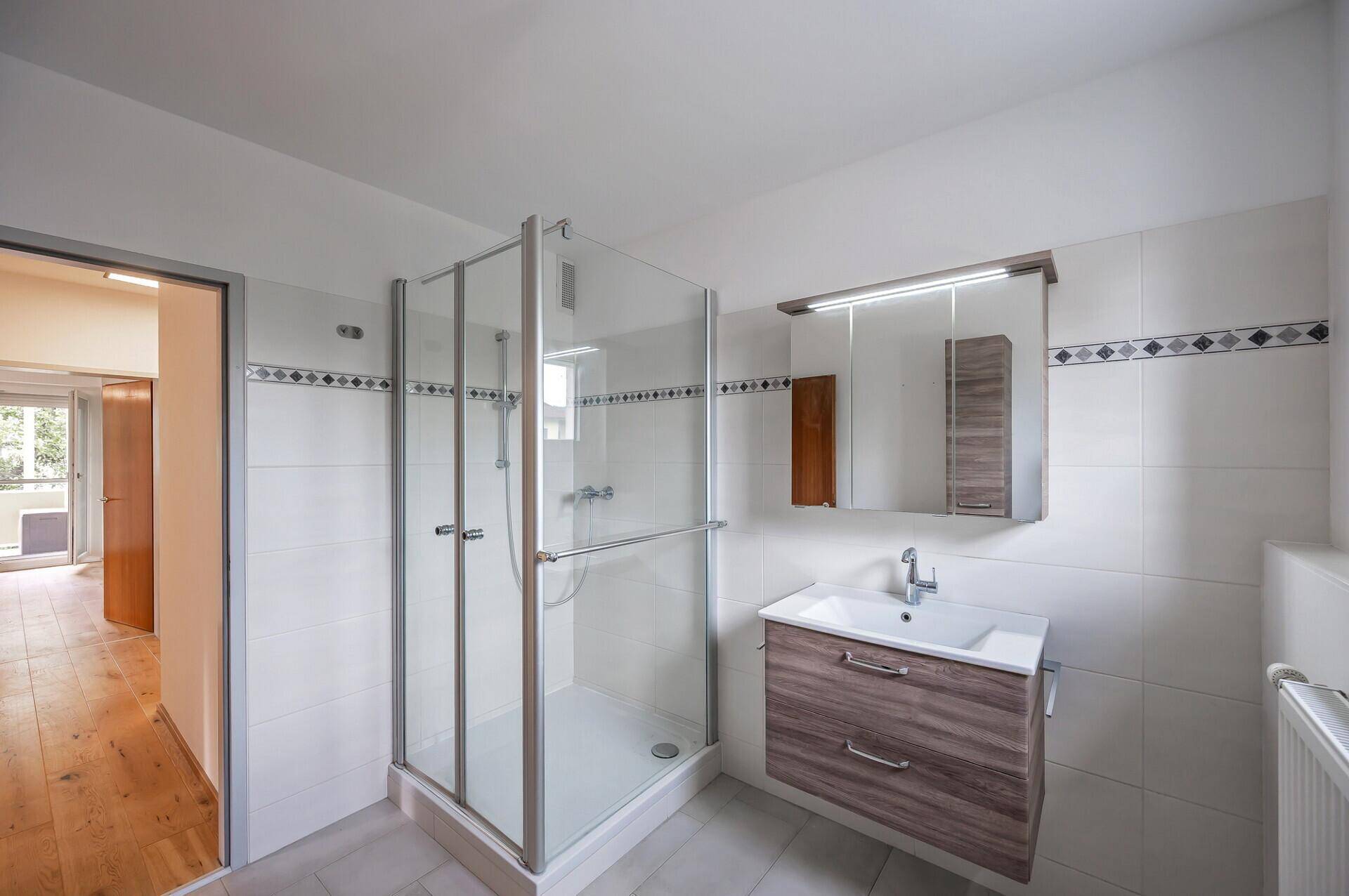 Badezimmer mit Duschkabine, Waschtisch und Spiegelschrank, hell gefliest.