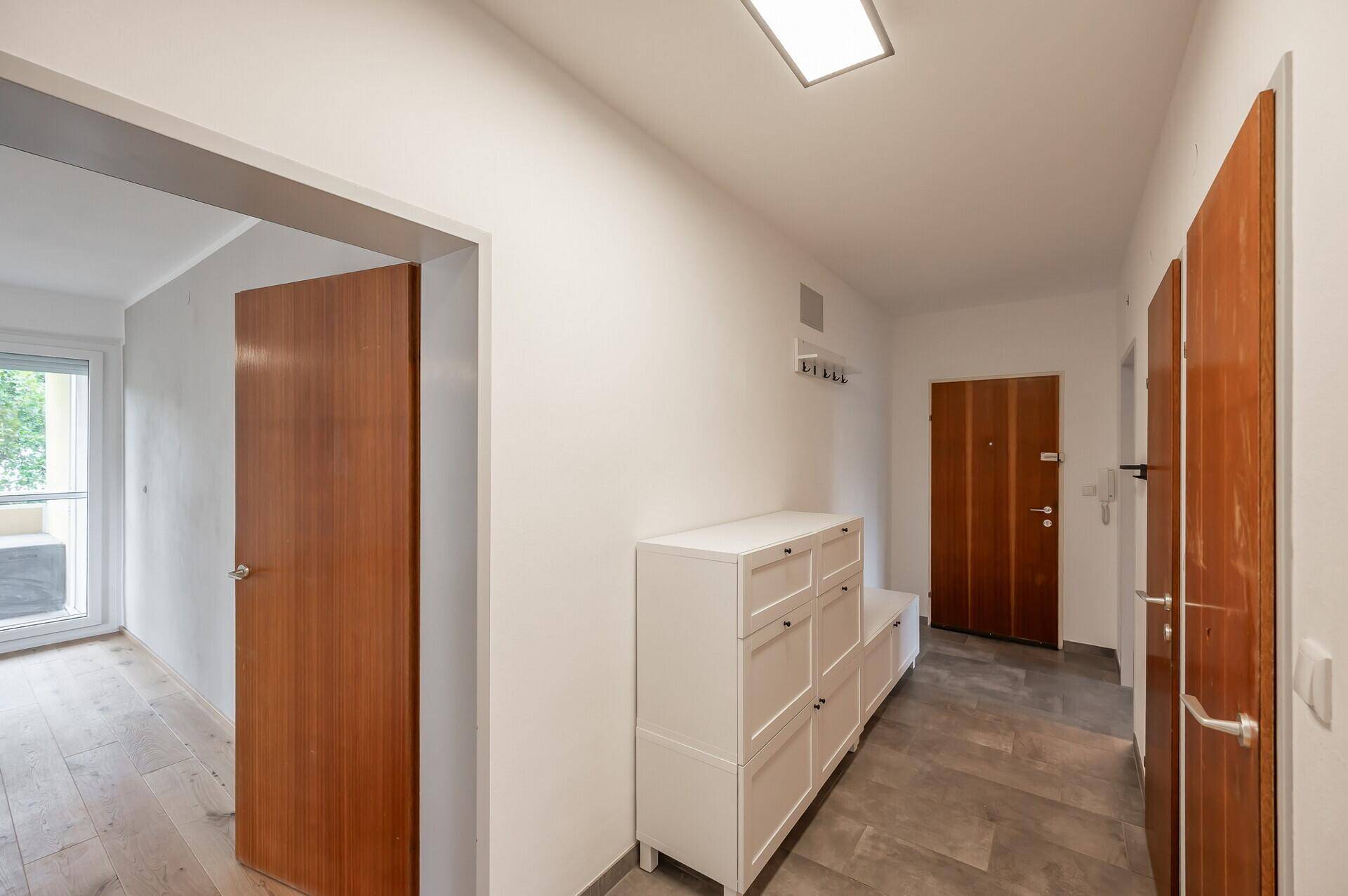 Eingangsbereich mit Fliesenboden, weißem Schuhschrank und Holztüren.