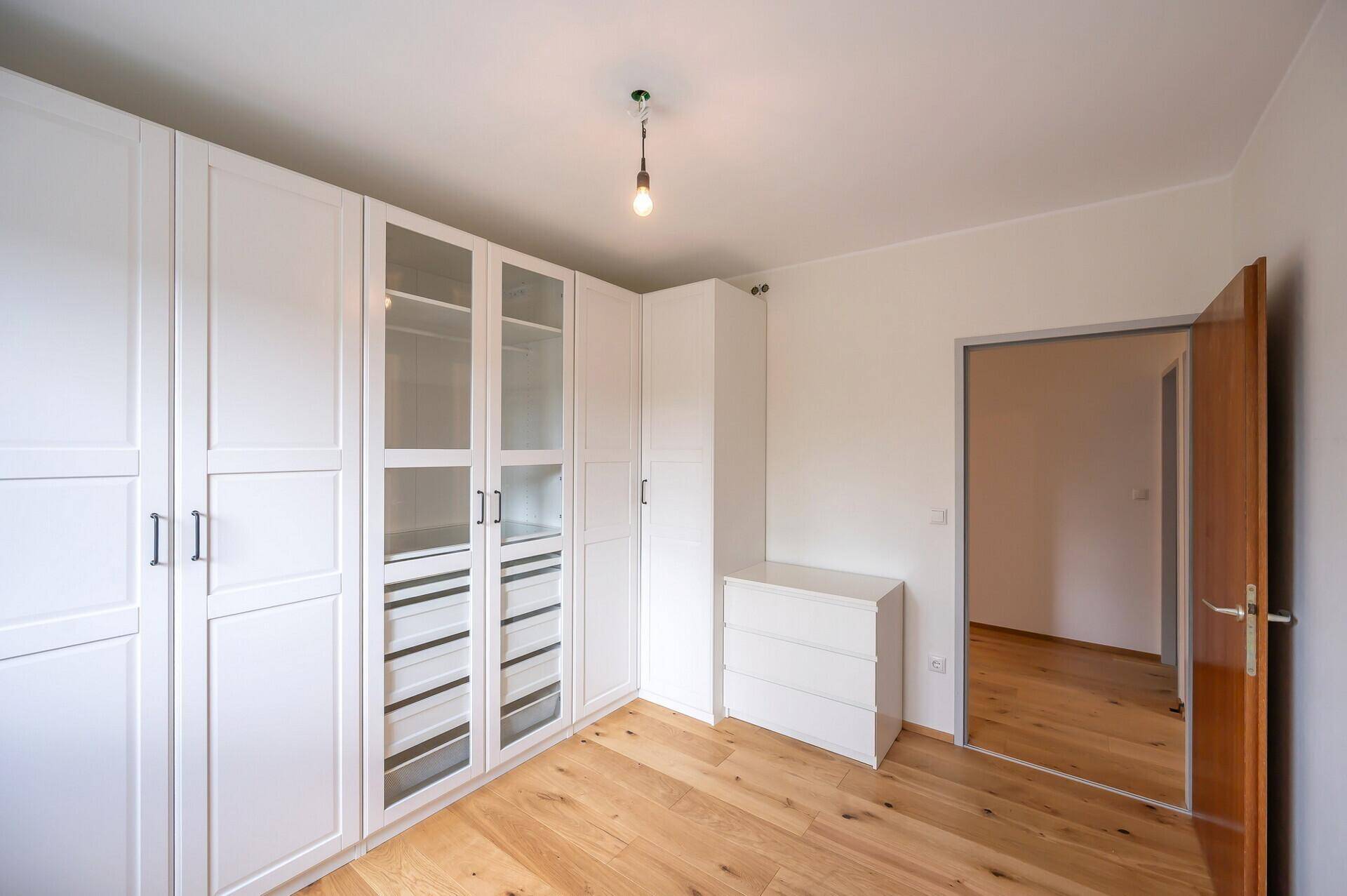 Schlafzimmer mit Parkettboden und geräumigem weißen Kleiderschrank.