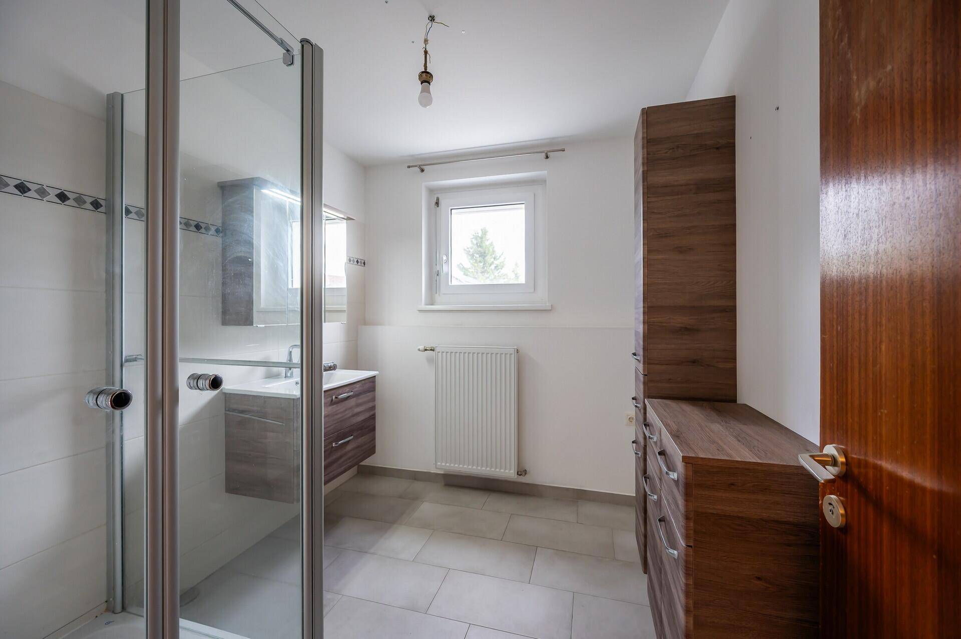Badezimmer mit moderner Duschkabine, Holzwaschtisch und Fenster für Tageslicht.