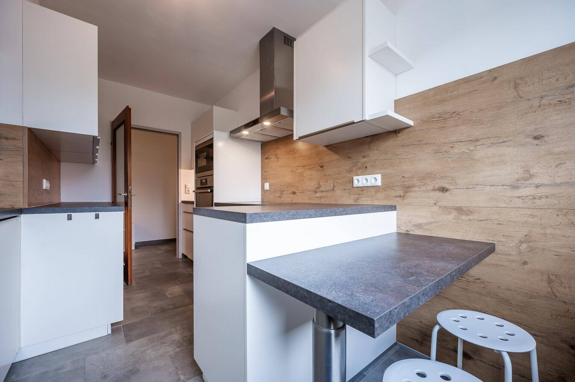 Moderne Küche mit weißen Schränken, Holzrückwand und praktischer Frühstückstheke.