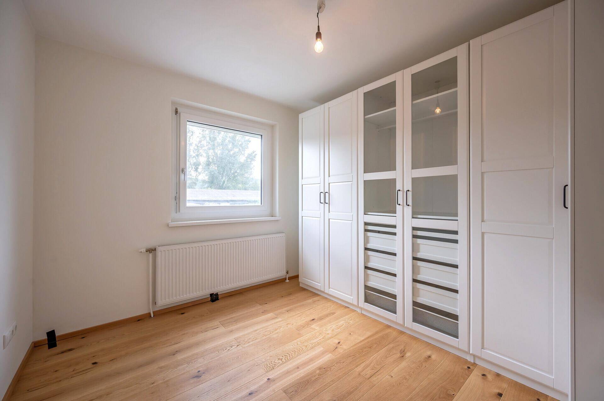 Schlafzimmer mit hellem Parkettboden, großem Kleiderschrank und Fenster.