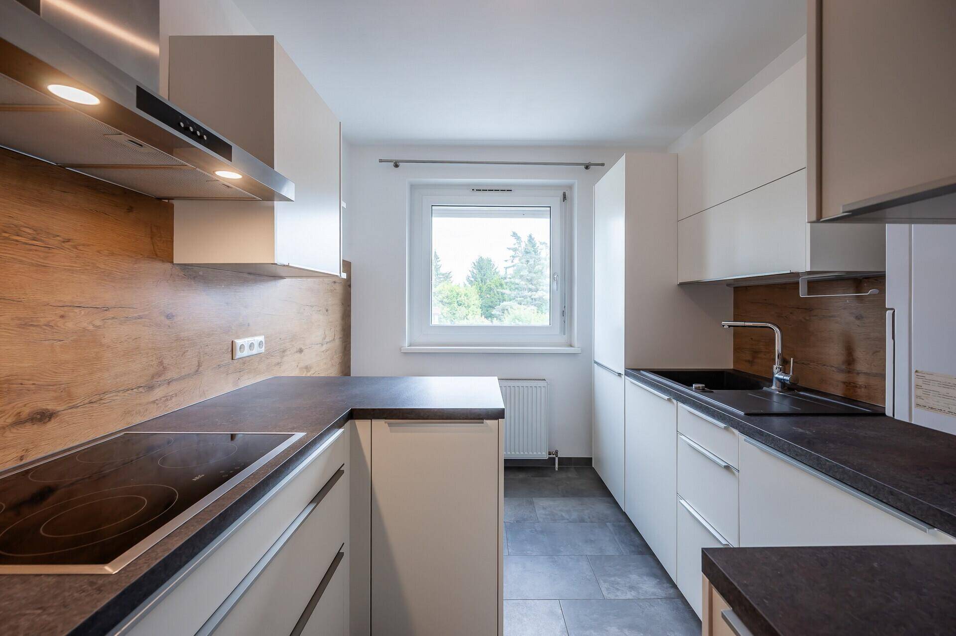 Moderne Küche mit Induktionskochfeld, Spüle und Dunstabzugshaube unter dem Fenster.