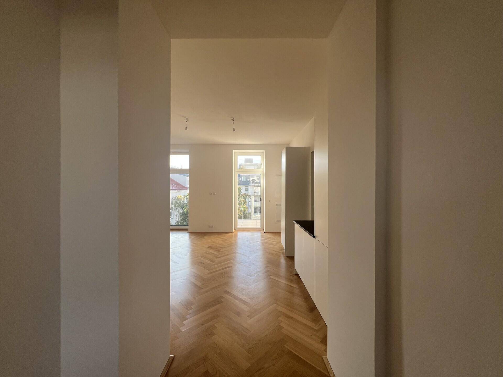 Blick vom Flur in den offenen Wohnbereich mit integrierter Küche und Fischgrätparkett.
