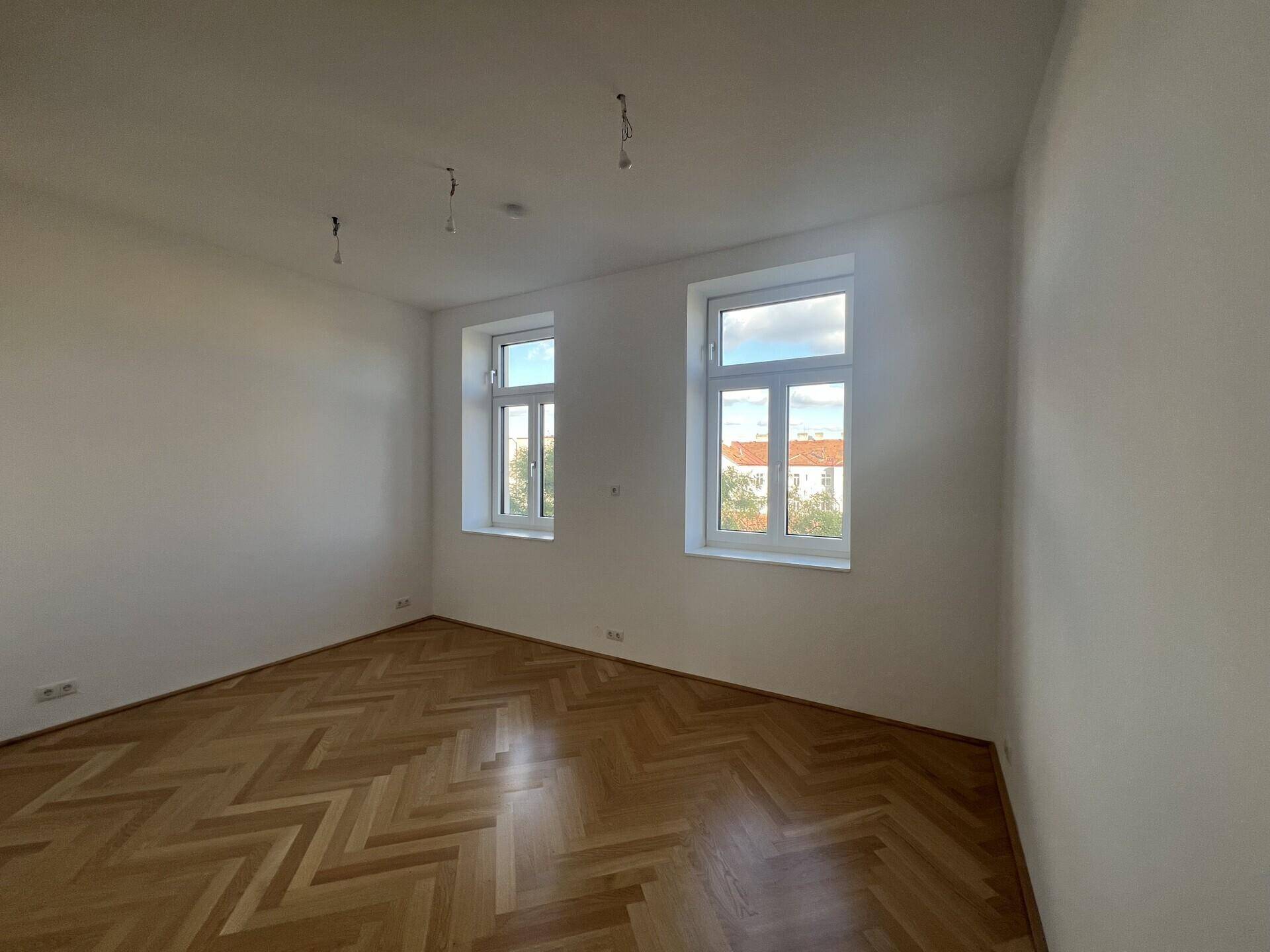 Heller Raum mit Fischgrätparkett und großen Fenstern, ideal für Schlaf- oder Arbeitszimmer.