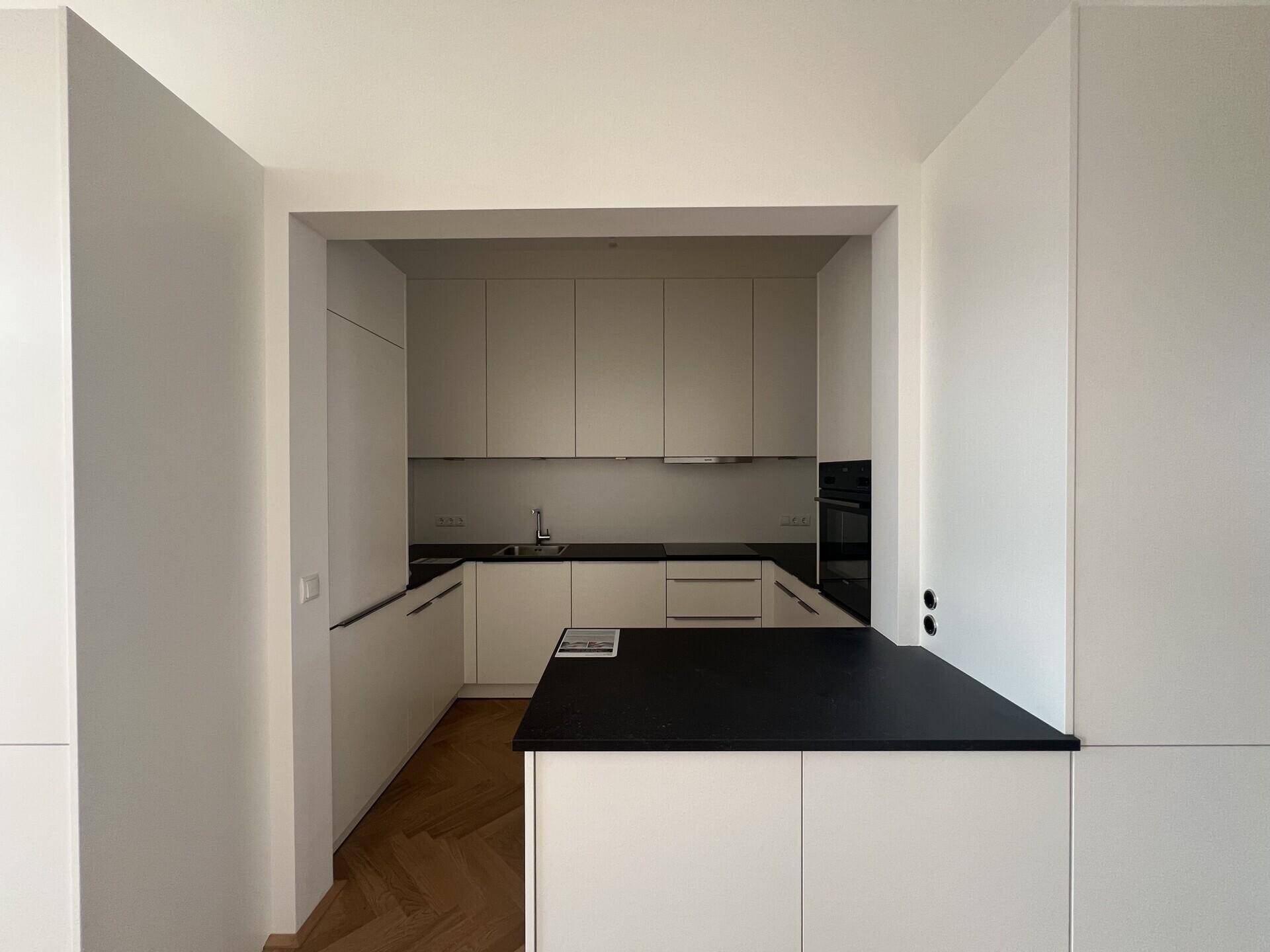 Moderne Einbauküche mit weißen Schränken, schwarzen Arbeitsplatten und integrierten Geräten.
