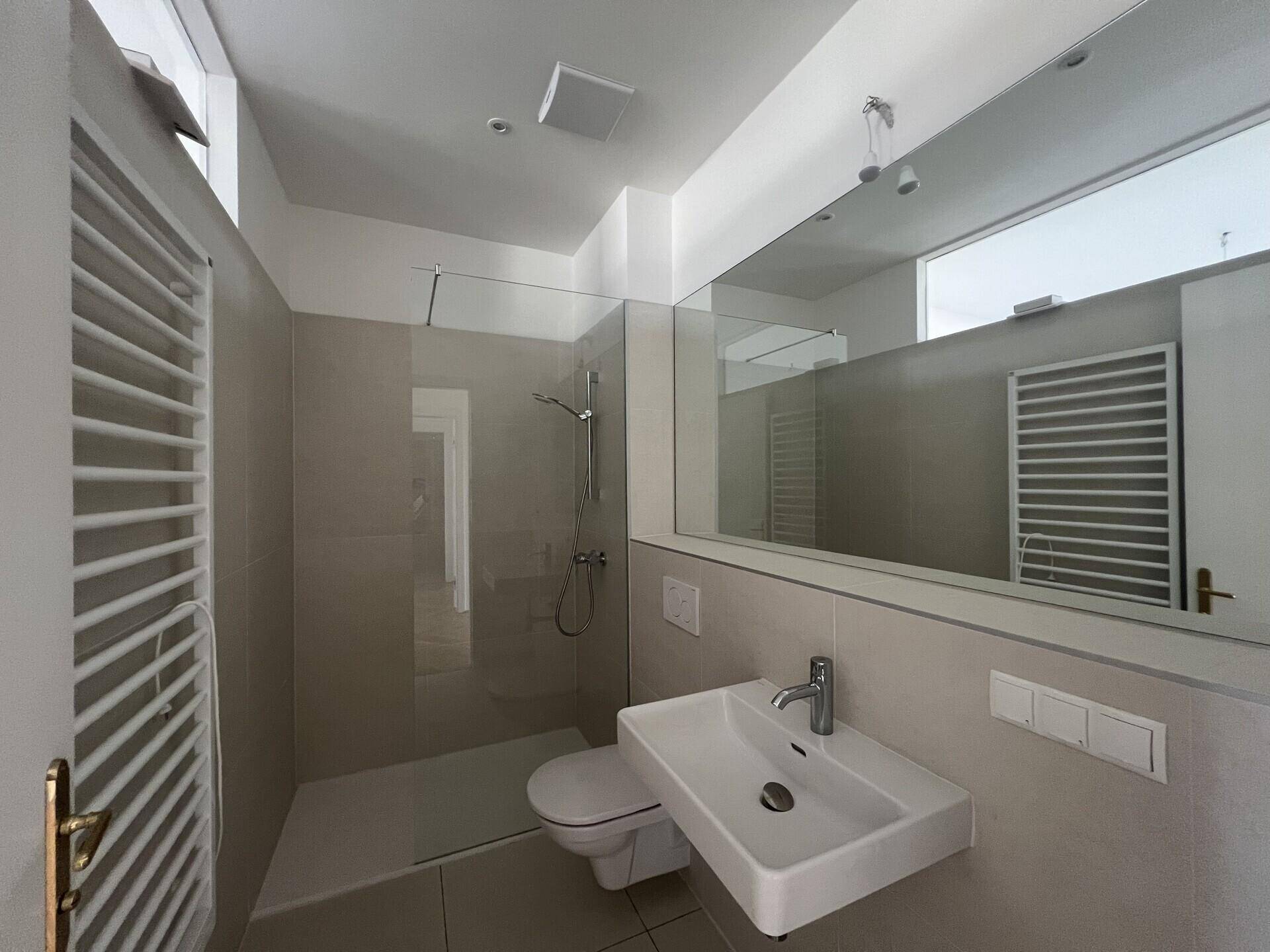 Modernes Badezimmer mit ebenerdiger Dusche, WC, Waschbecken und Handtuchheizkörper.