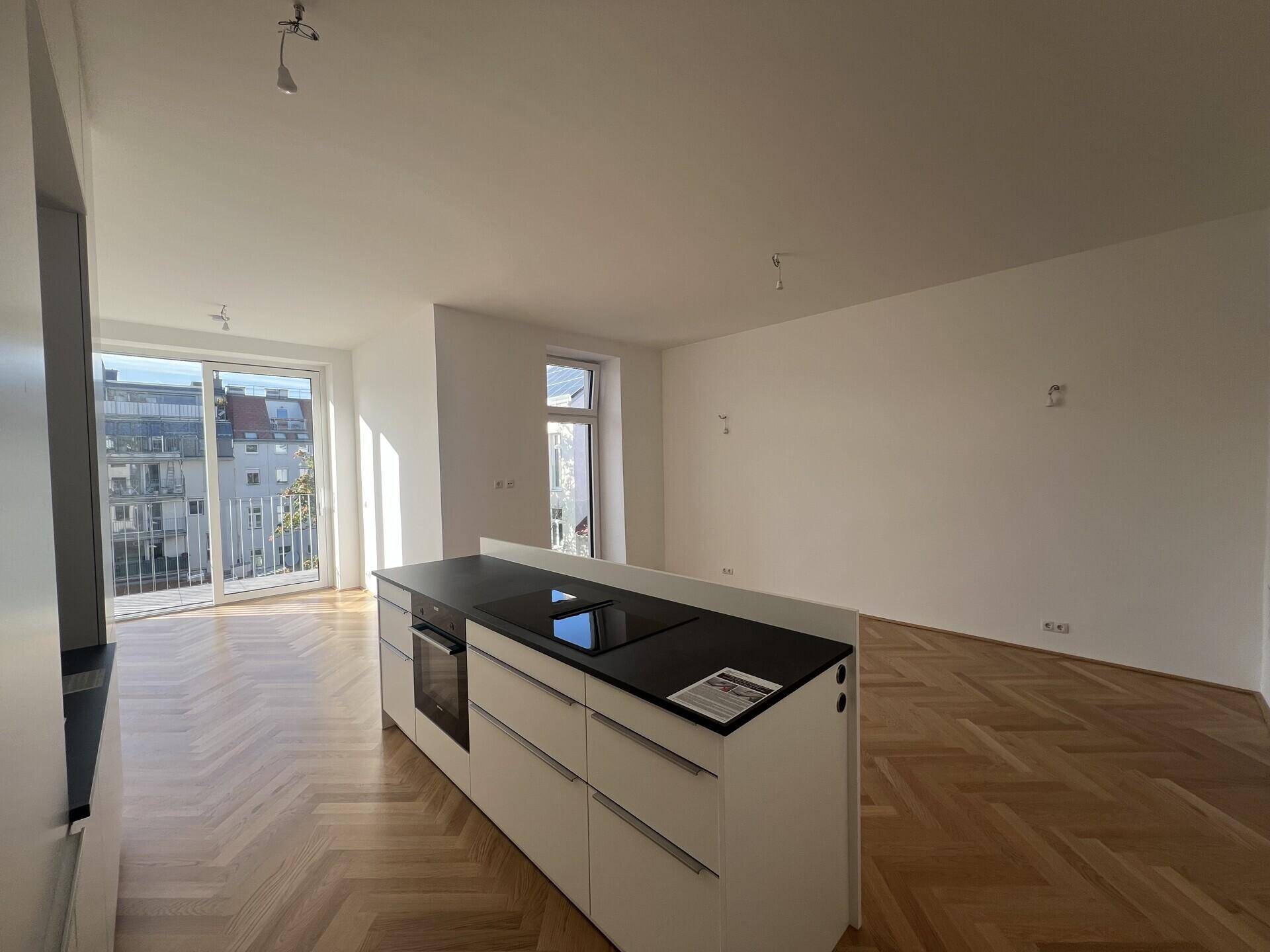 Geräumige Wohnküche mit Kücheninsel, integriertem Backofen und Induktionskochfeld auf Fischgrätparkett.