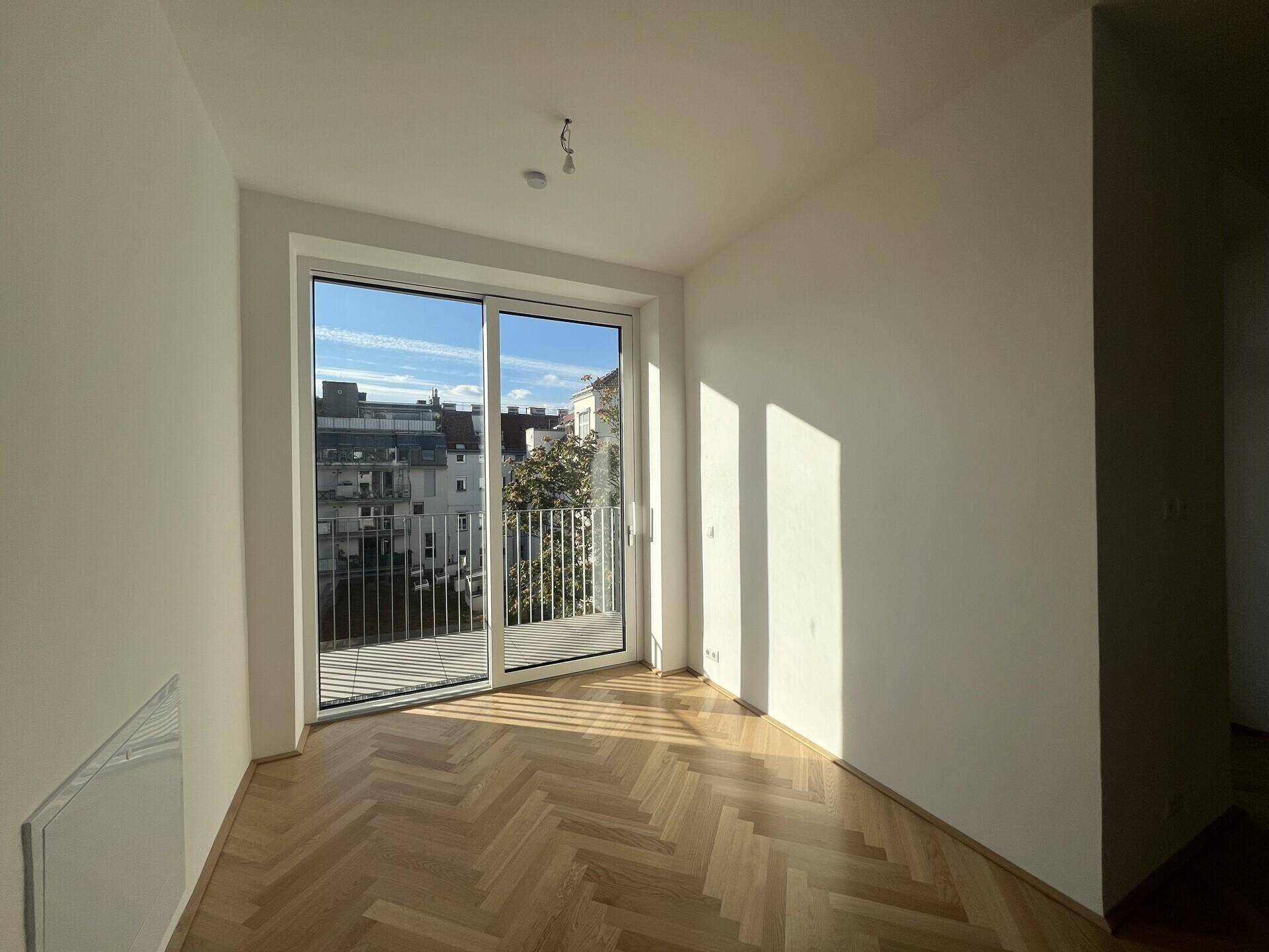 Sonniger Wohnbereich mit elegantem Fischgrätparkett und großem Fenster mit Blick auf die Stadt.