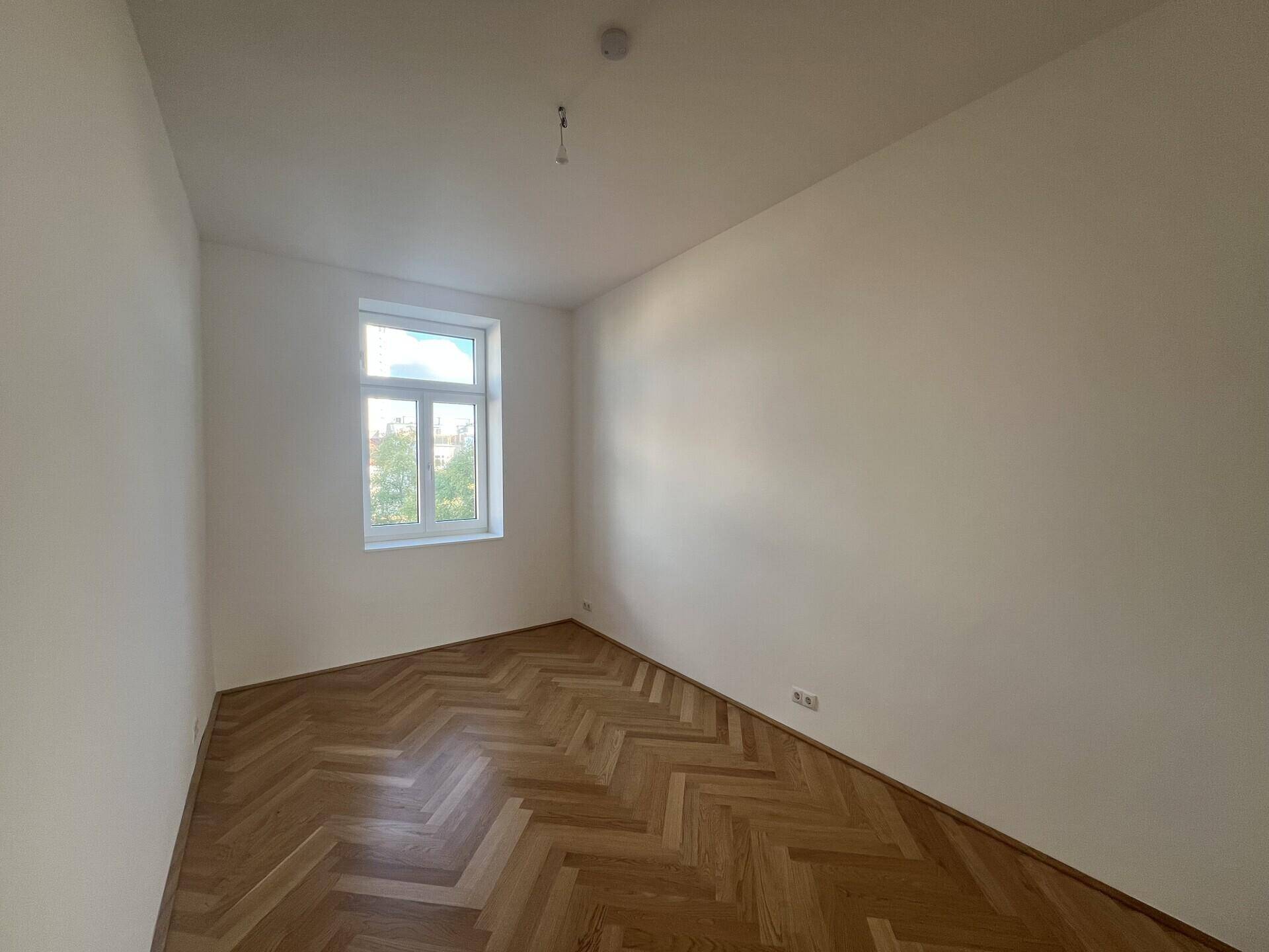 Gemütliches Zimmer mit einem Fenster und klassischem Fischgrätparkett, ideal als Kinder- oder Arbeitszimmer.
