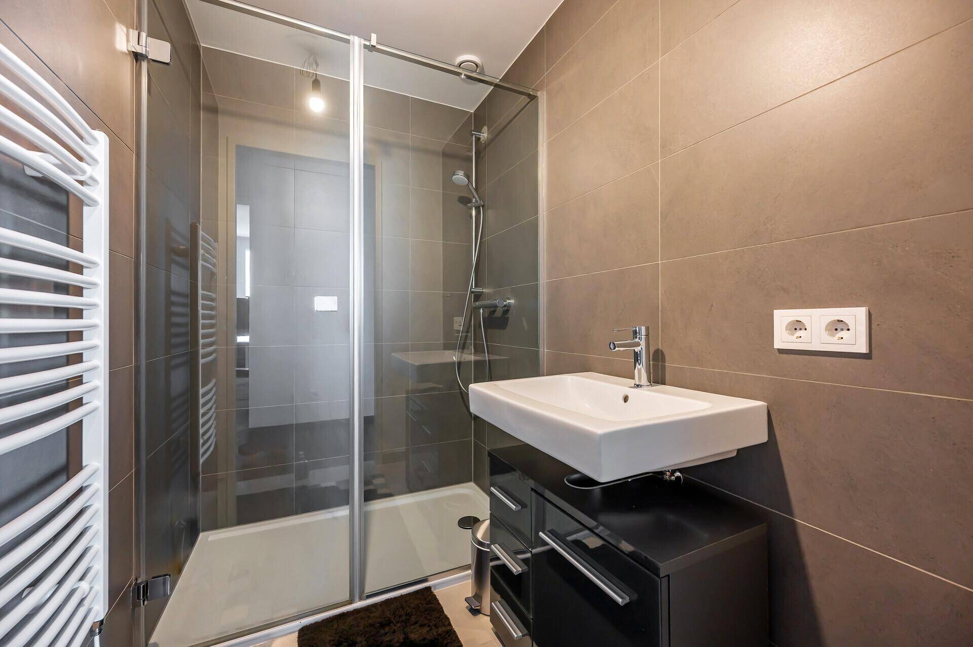 Badezimmer mit moderner Duschkabine, Einzelwaschbecken und beheiztem Handtuchhalter.