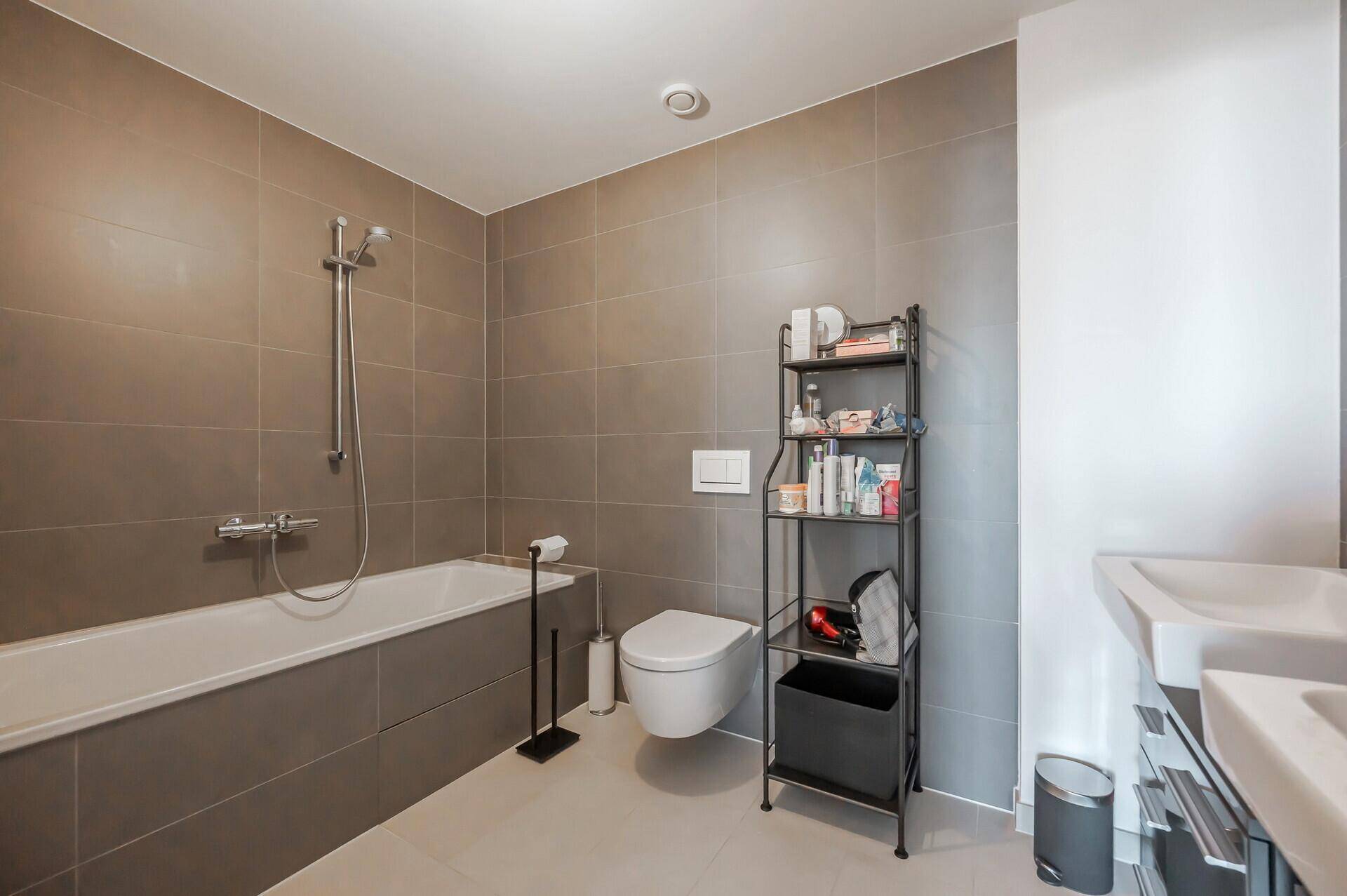 Modernes Badezimmer mit Badewanne, Wand-WC und großformatigen Fliesen in Grautönen.