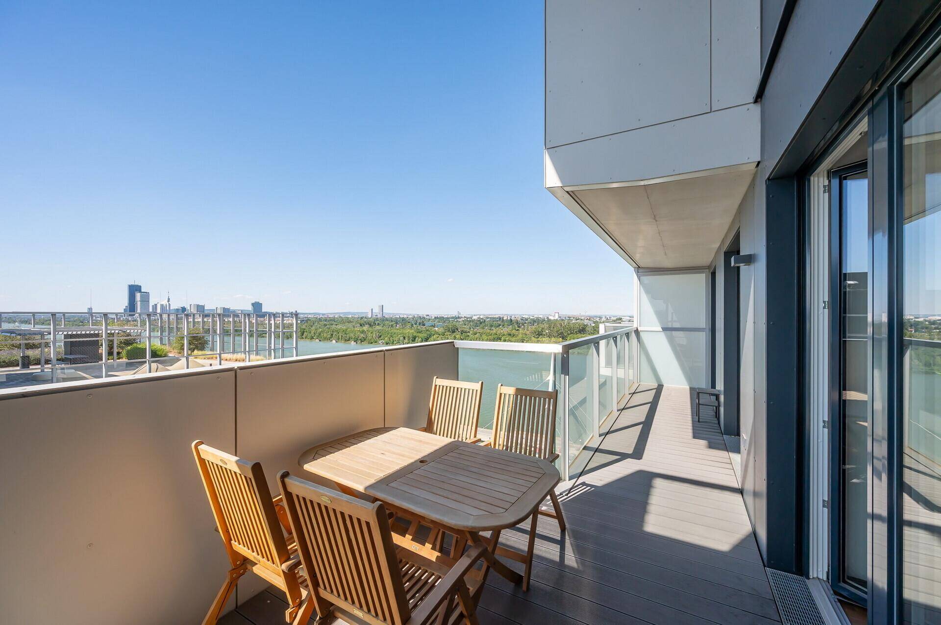 Geräumiger Balkon mit Holztisch und Stühlen, bietet einen weiten Blick auf die Donau.