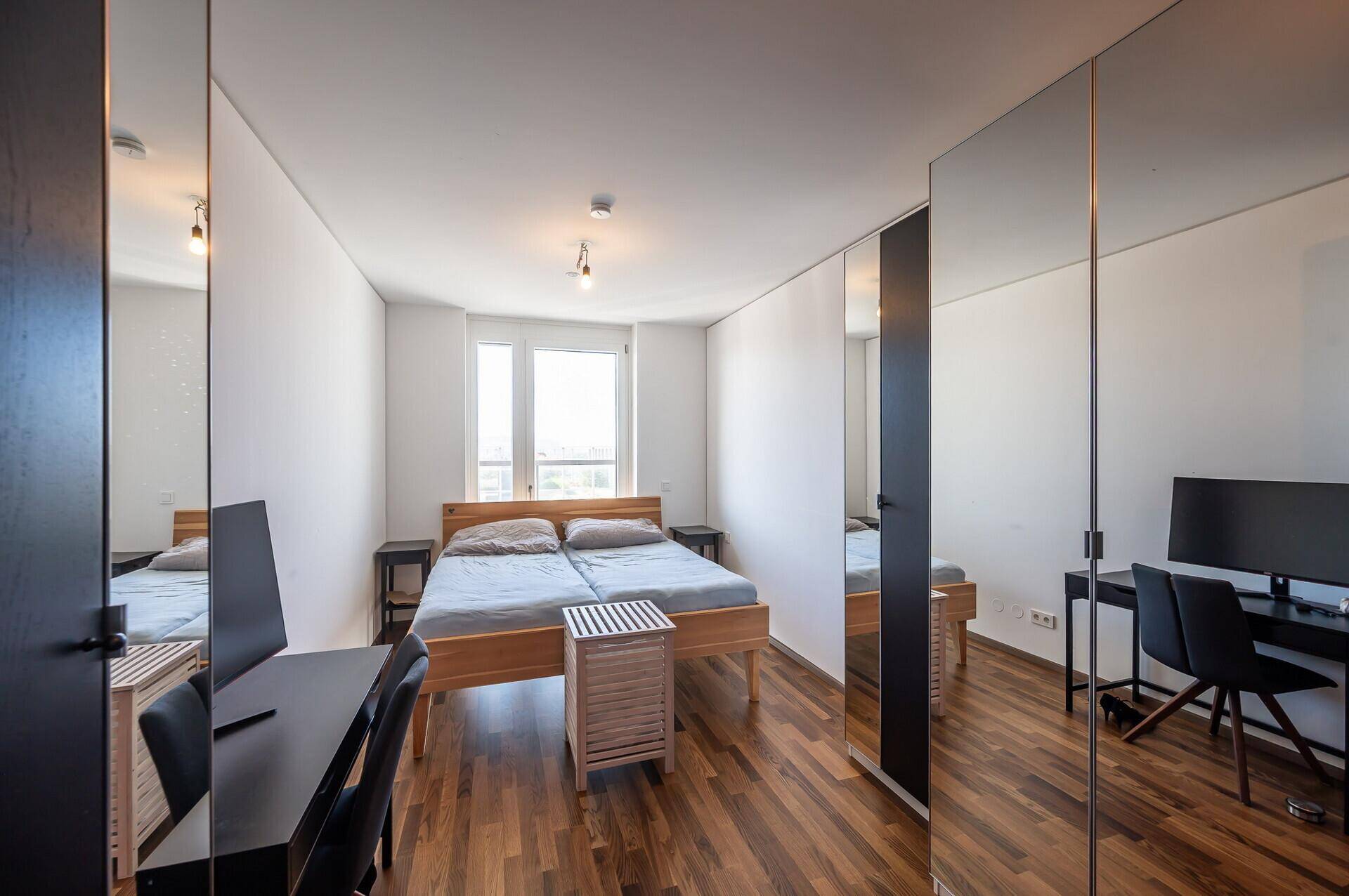 Schlafzimmer mit Holzbett, Schreibtisch und großen Spiegelschränken, hell und funktional.