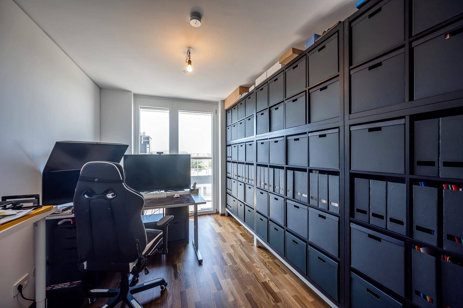 Funktionales Arbeitszimmer mit Schreibtisch, Computer und umfangreichen Regalsystemen für Stauraum.