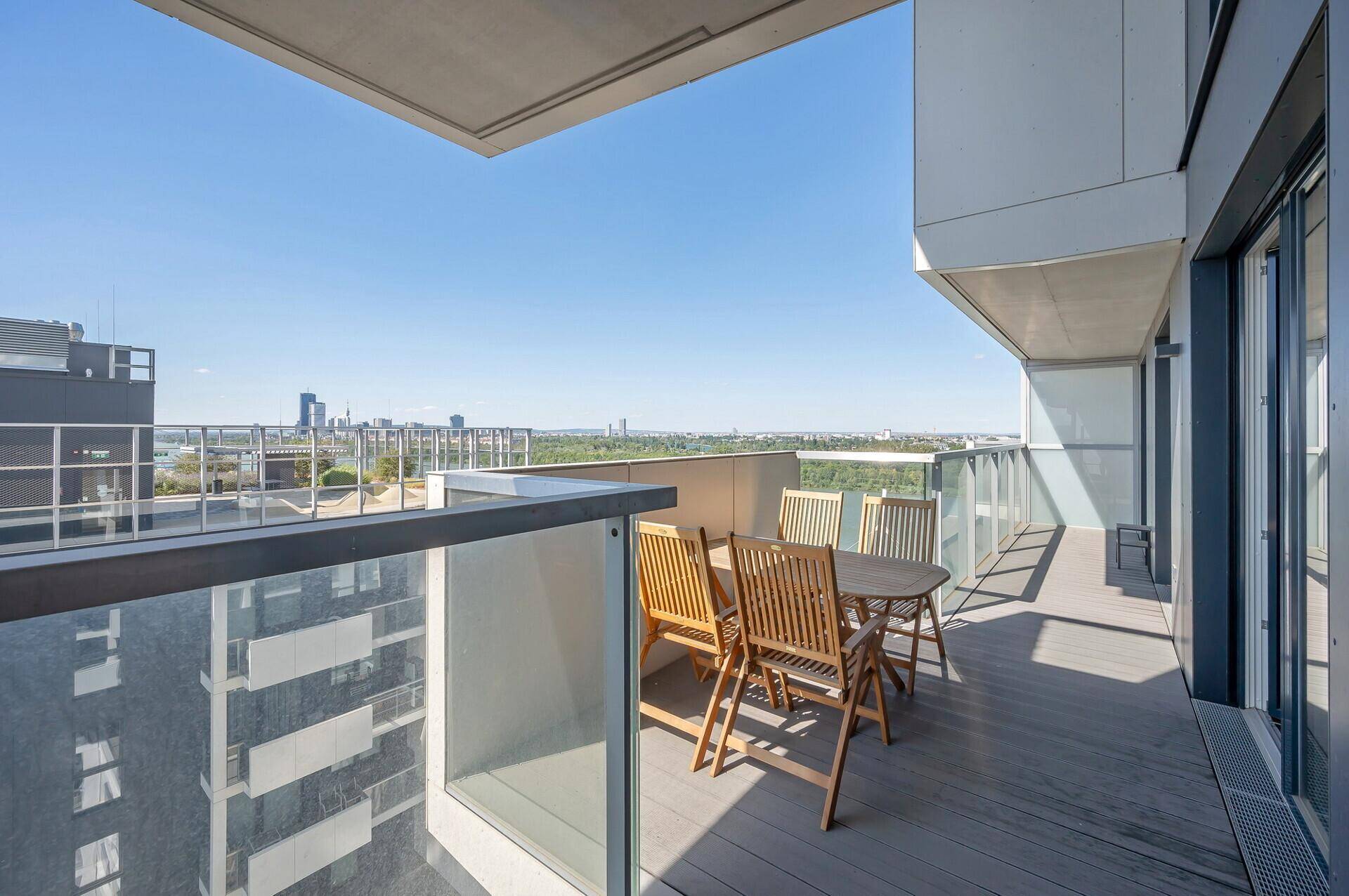 Heller Balkon mit Glasgeländer und Holzmöbeln, ideal für entspannte Stunden mit Flussblick.