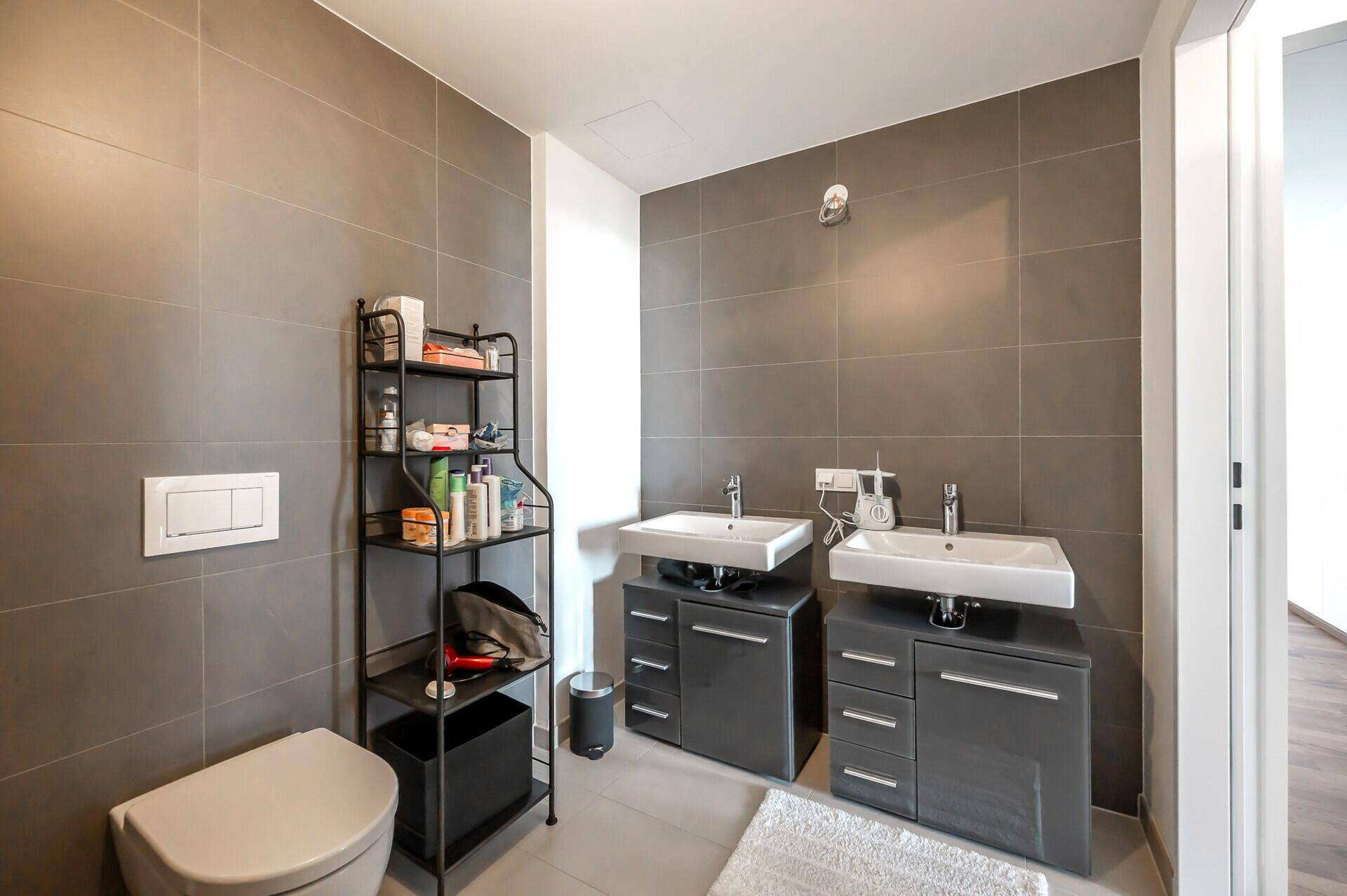 Badezimmer mit Doppelwaschbecken, Wand-WC und modernen grauen Fliesen.