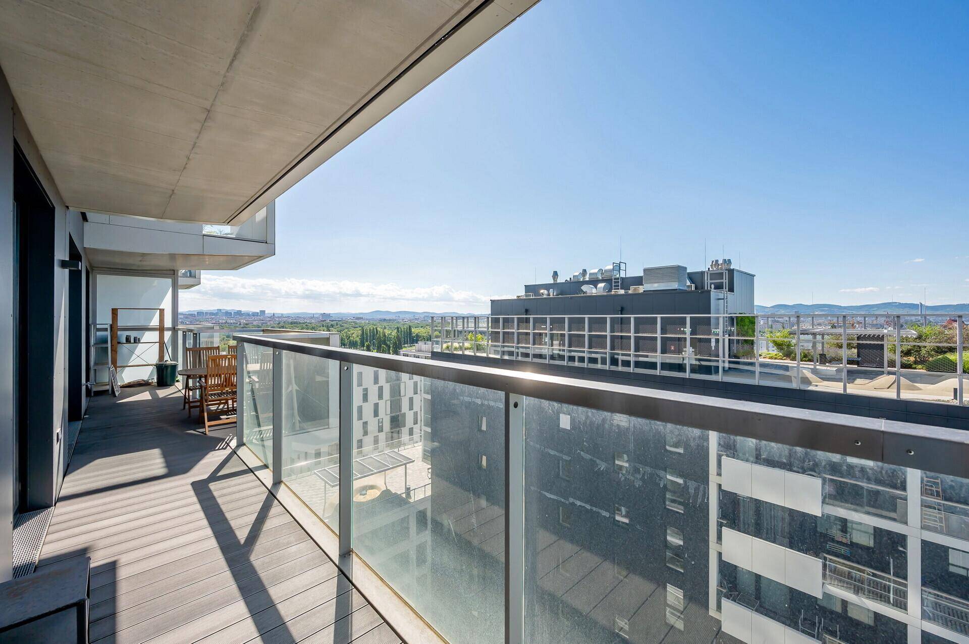 Langer Balkon mit modernem Glasgeländer und Blick auf die umliegenden Gebäude und die Landschaft.