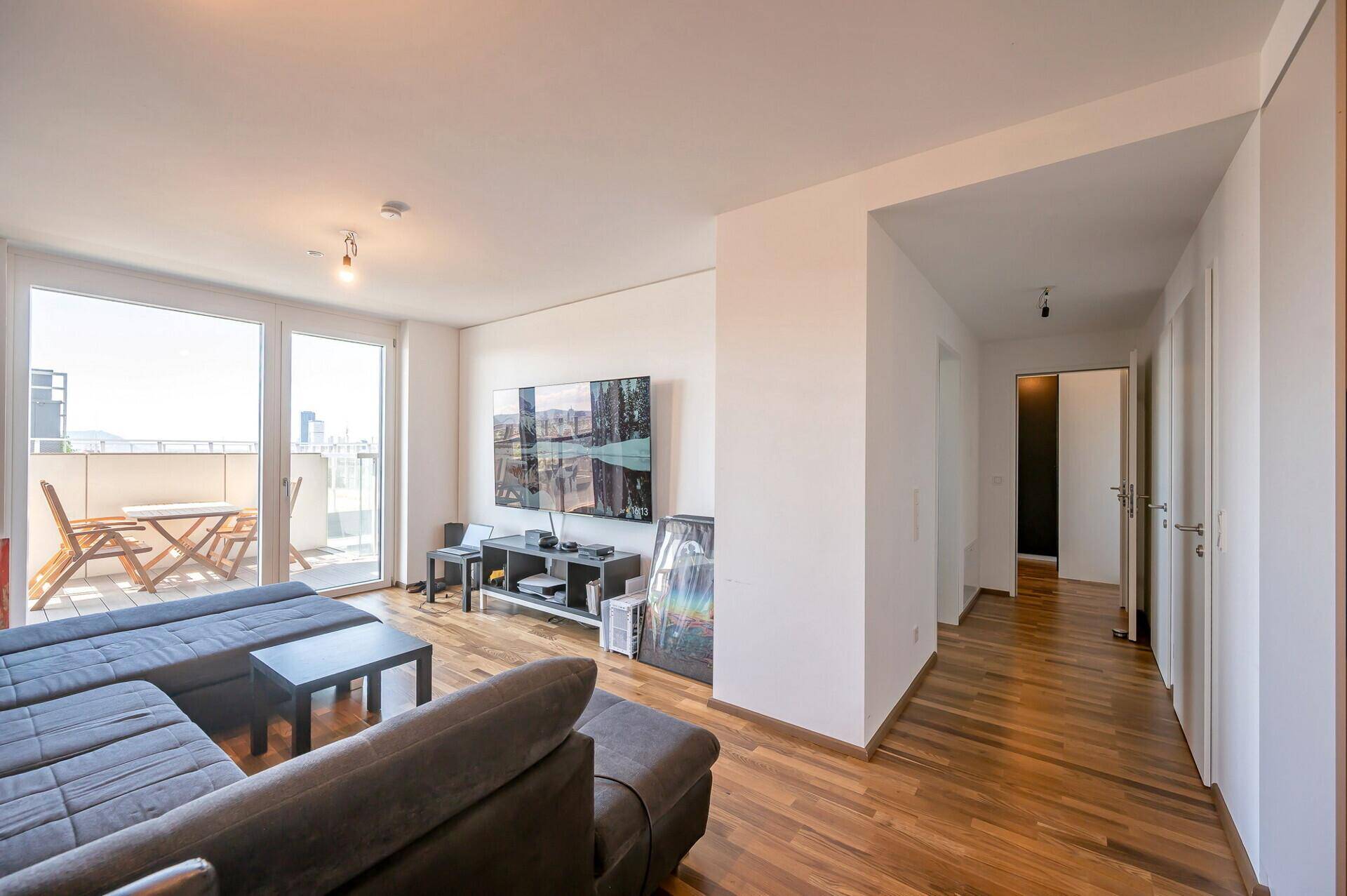 Helles Wohnzimmer mit Holzboden, großem Fernseher und direktem Zugang zum Balkon.
