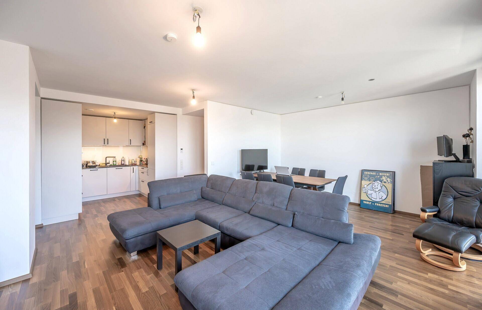 Wohnbereich mit integrierter Küchenzeile, großem Sofa und Holzboden in modernem Stil.