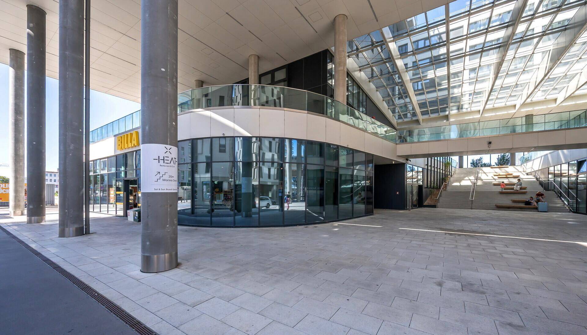 Moderne Architektur mit Glasfassade und großen Säulen in einem städtischen Umfeld.