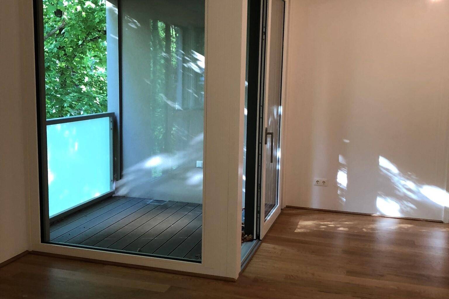 Heller Raum mit Holzboden und großem Zugang zu einem Balkon, der viel Tageslicht hereinlässt.