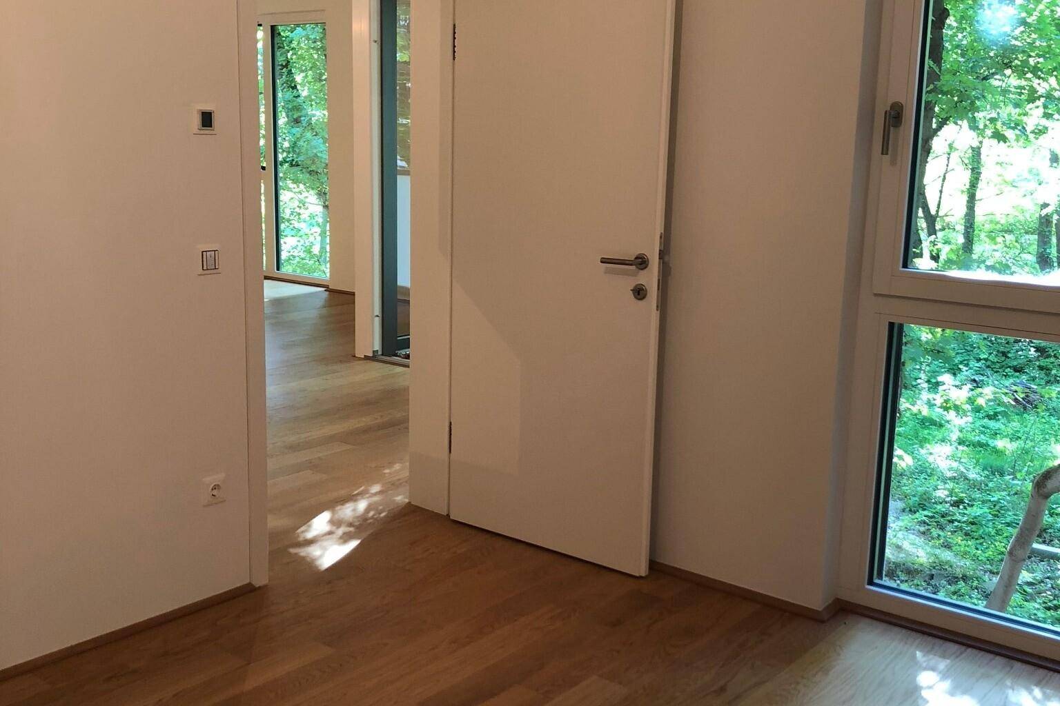 Heller Flur mit Holzboden und Blick ins Grüne durch große Fenster, die viel Licht spenden.