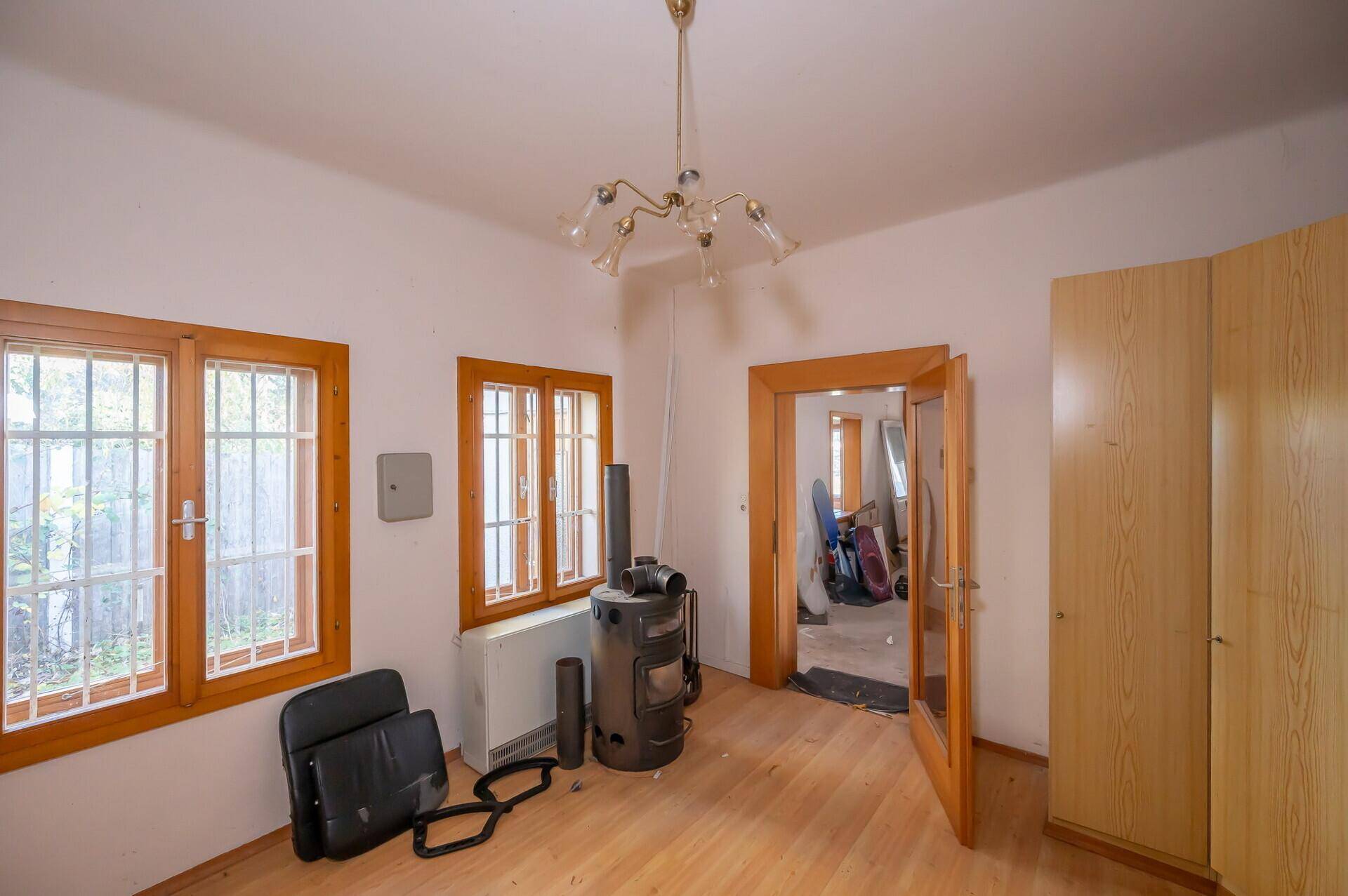 Zimmer mit Holzboden, Fenstern und einem Holzofen, bereit für die Renovierung.