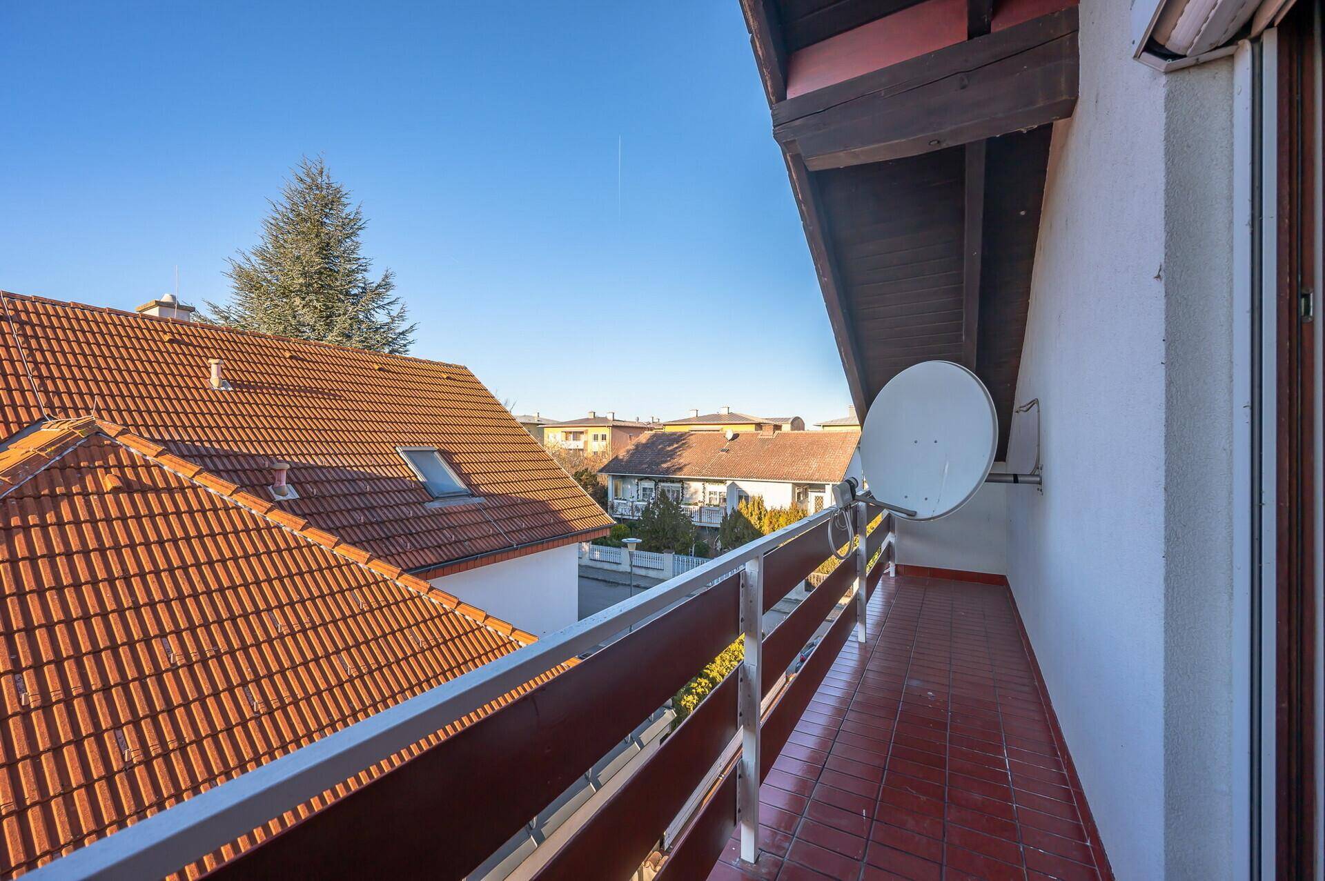 Balkon mit roten Fliesen und Blick über die Dächer der Nachbarhäuser unter blauem Himmel.