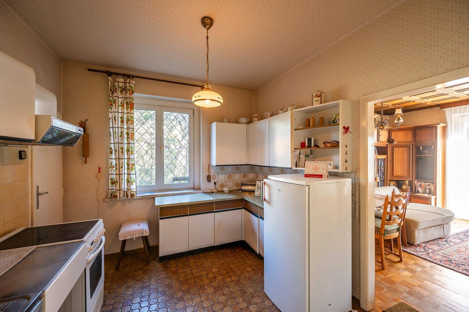 Helle Küche mit Fenster, älteren Geräten und gemustertem Boden, mit Blick ins Grüne.