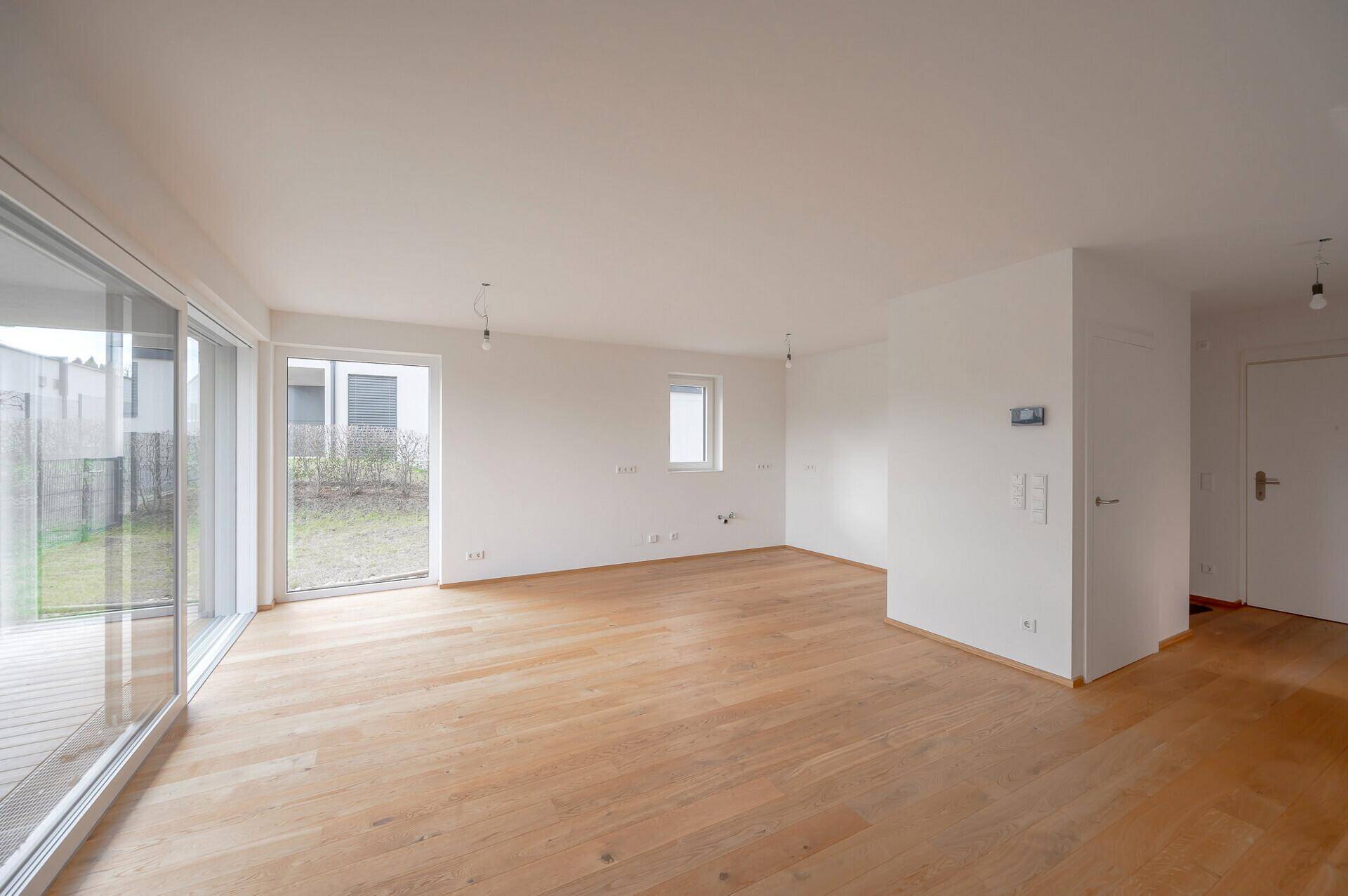 Geräumiges, leeres Wohnzimmer mit hellem Parkettboden und großen Fenstern zum Garten.