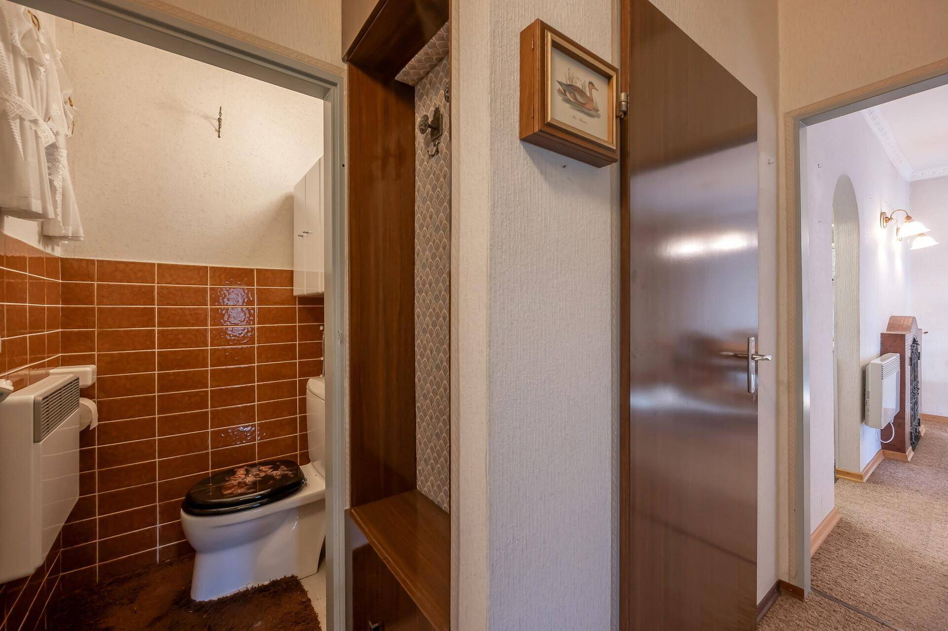 Separate Toilette mit braunen Fliesen und einfacher Ausstattung, neben einem Garderobenbereich.