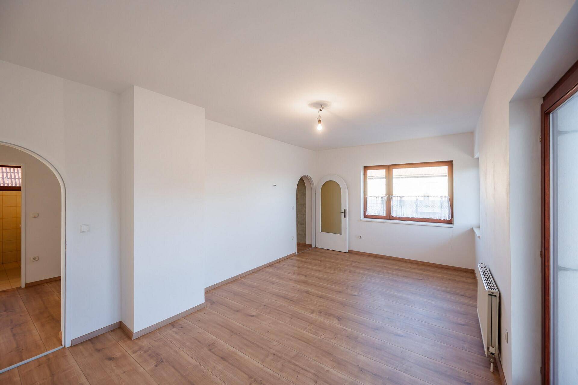 Geräumiges Wohnzimmer mit Holzboden, weißen Wänden und einem eleganten Rundbogen.