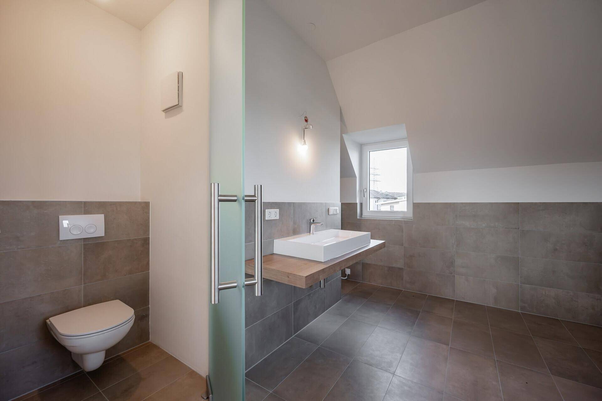 Modernes Badezimmer im Dachgeschoss mit Schräge, wandhängendem WC und Einzelwaschbecken.