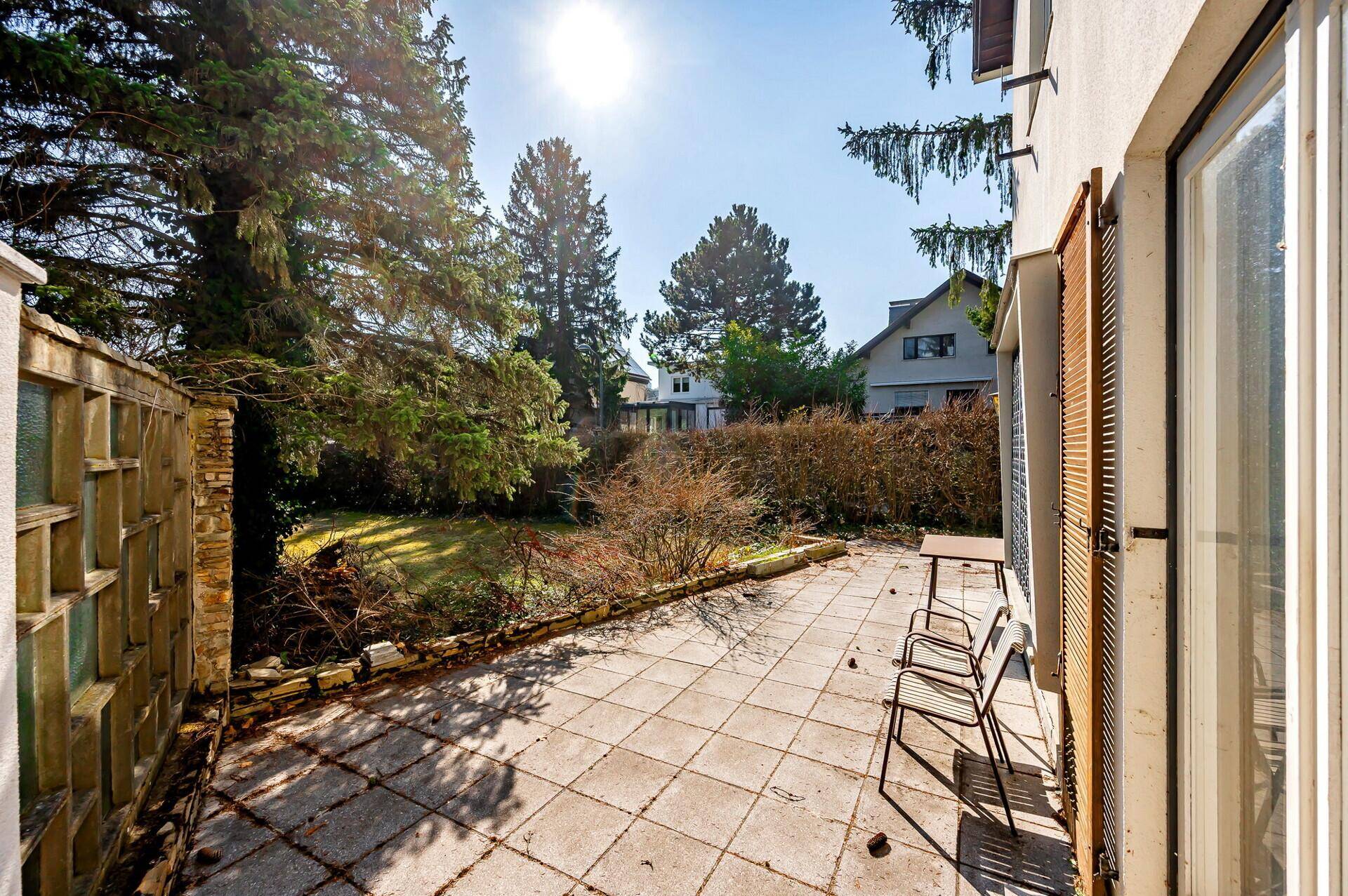 Sonniger Terrassenbereich mit Pflastersteinen und Gartenmöbeln, mit Blick auf den Garten.