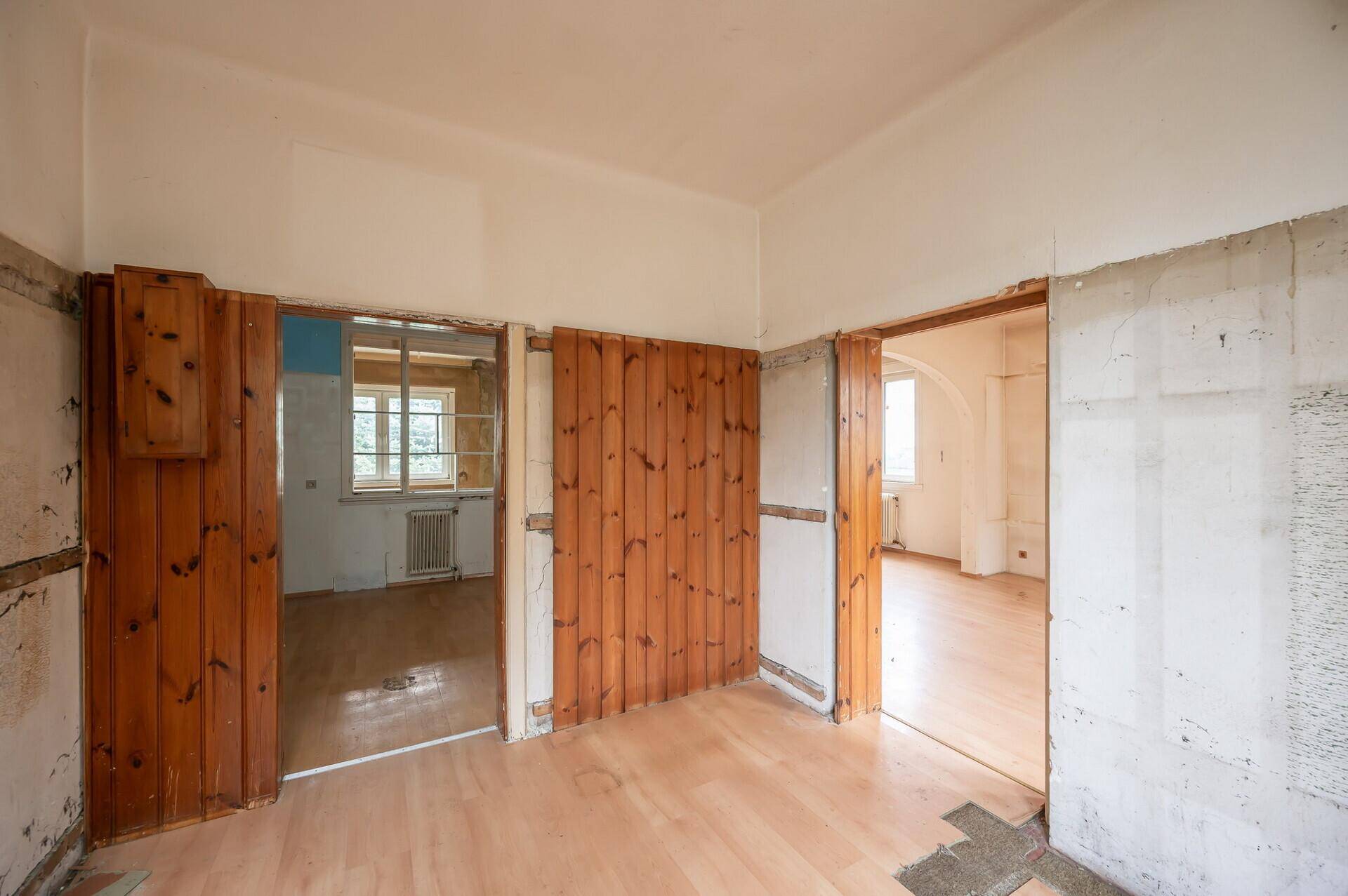 Renovierungsbedürftiger Raum mit Holzboden und teilweise entfernten Wandverkleidungen.