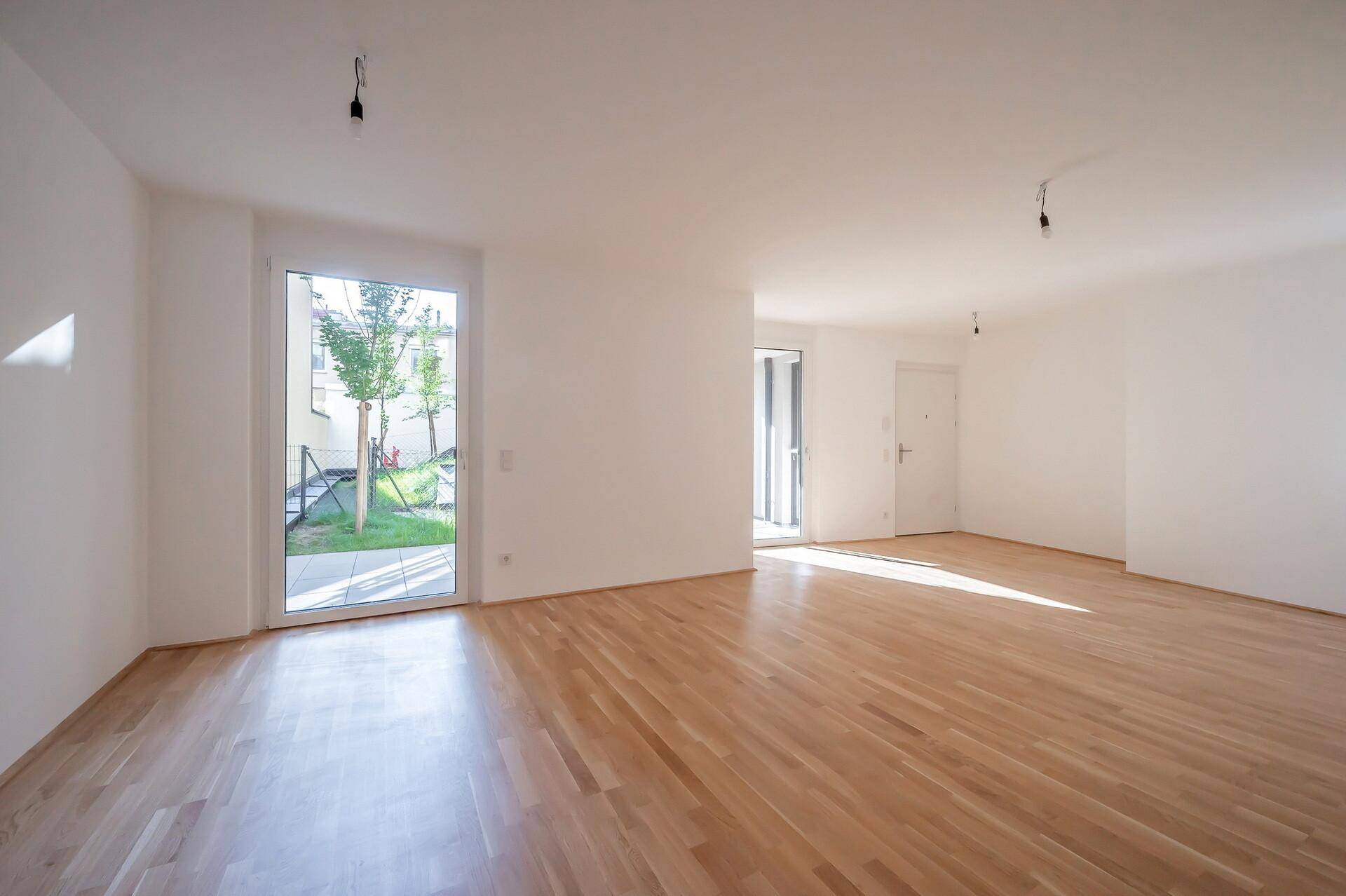 Heller, leerer Wohnraum mit Parkettboden und großer Terrassentür.