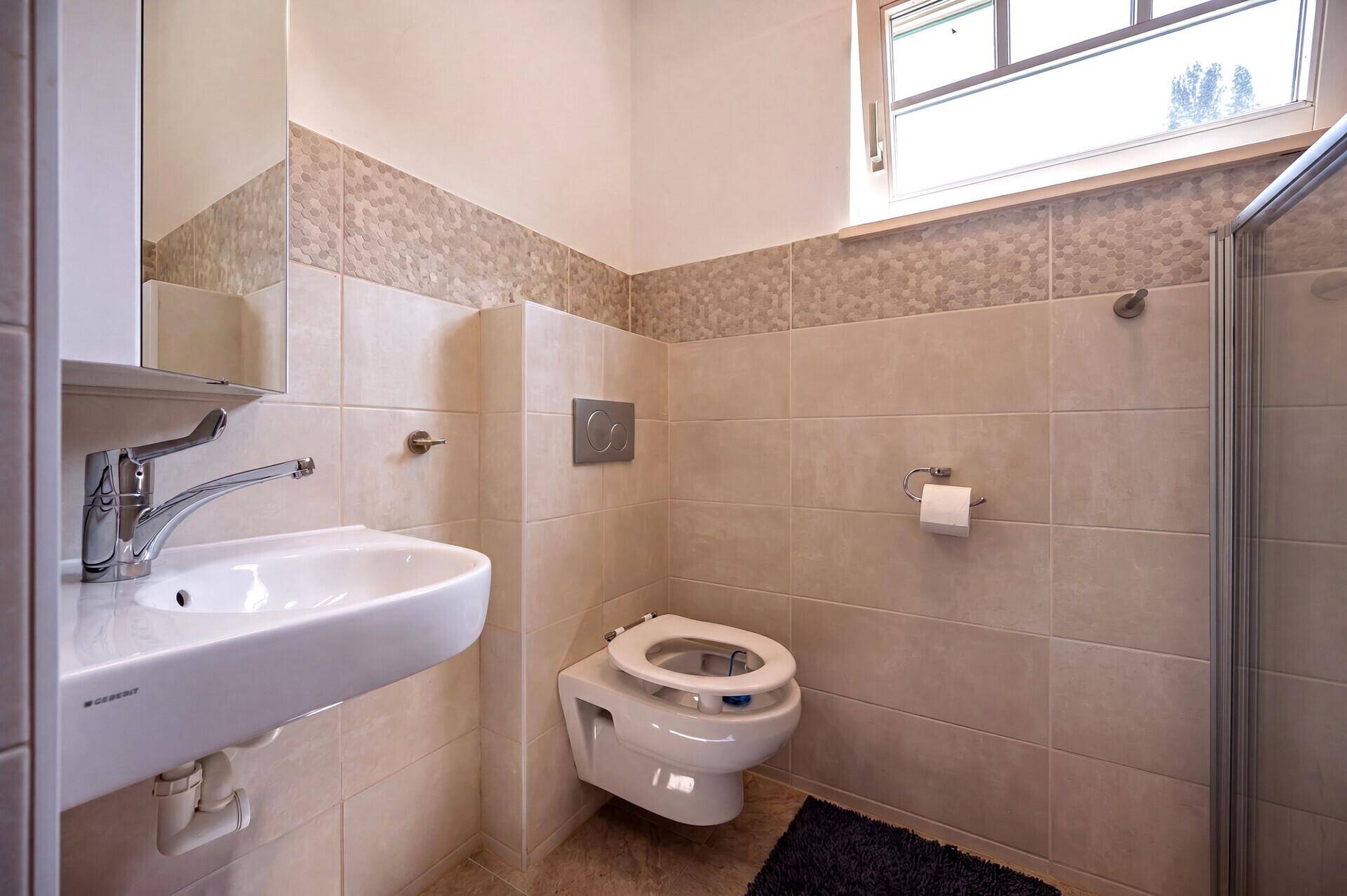 Funktionales Badezimmer mit Waschbecken, Wand-WC und Fenster für Tageslicht.