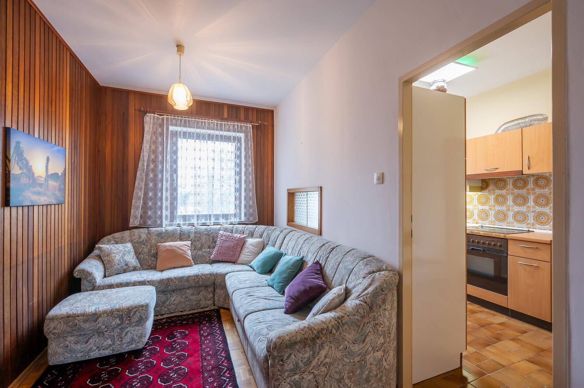 Gemütliches Wohnzimmer mit Ecksofa, Holzvertäfelung und Blick in die Küche.