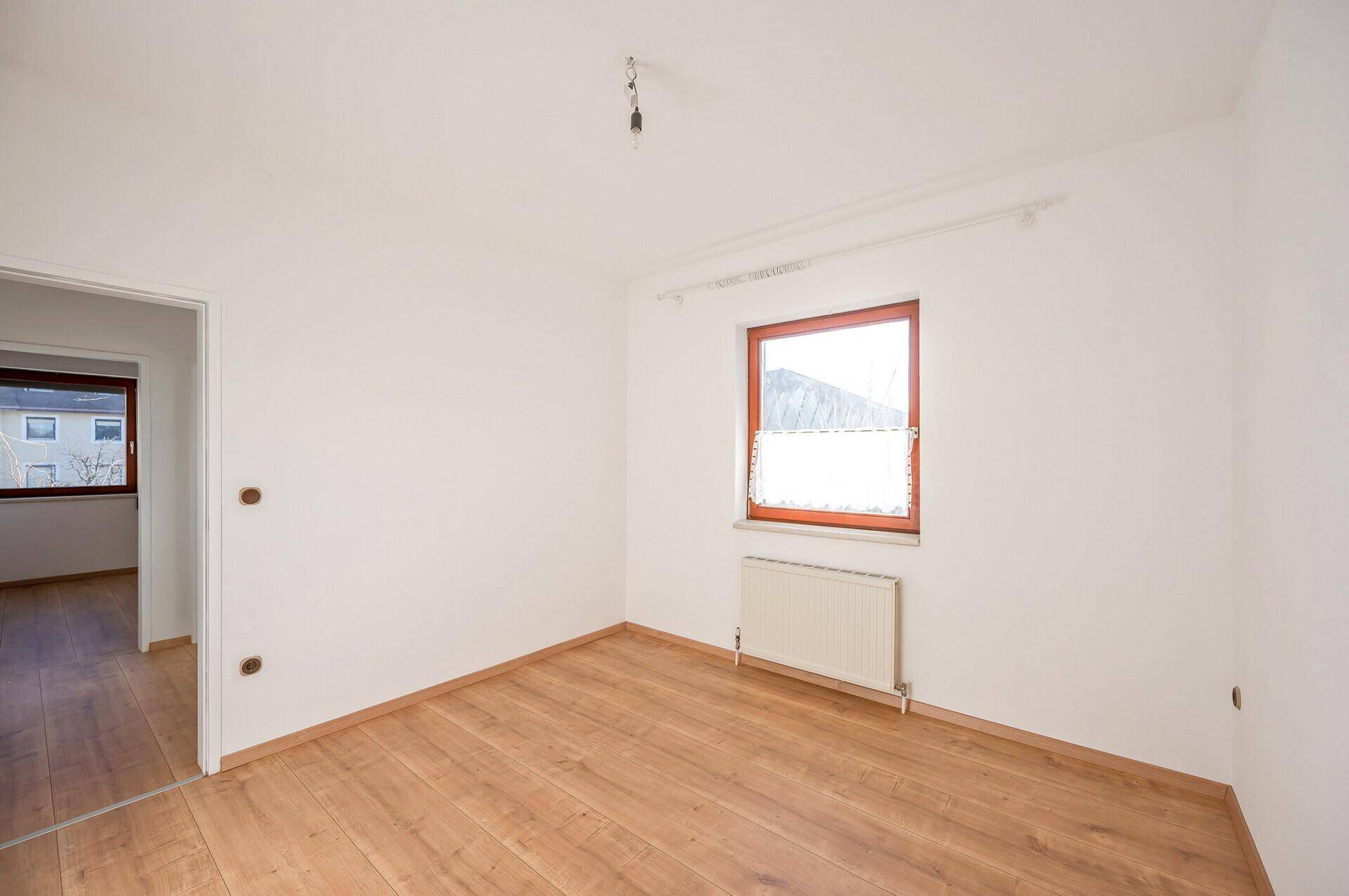 Helles Schlafzimmer mit Holzboden, weißen Wänden und einem Fenster mit Ausblick.
