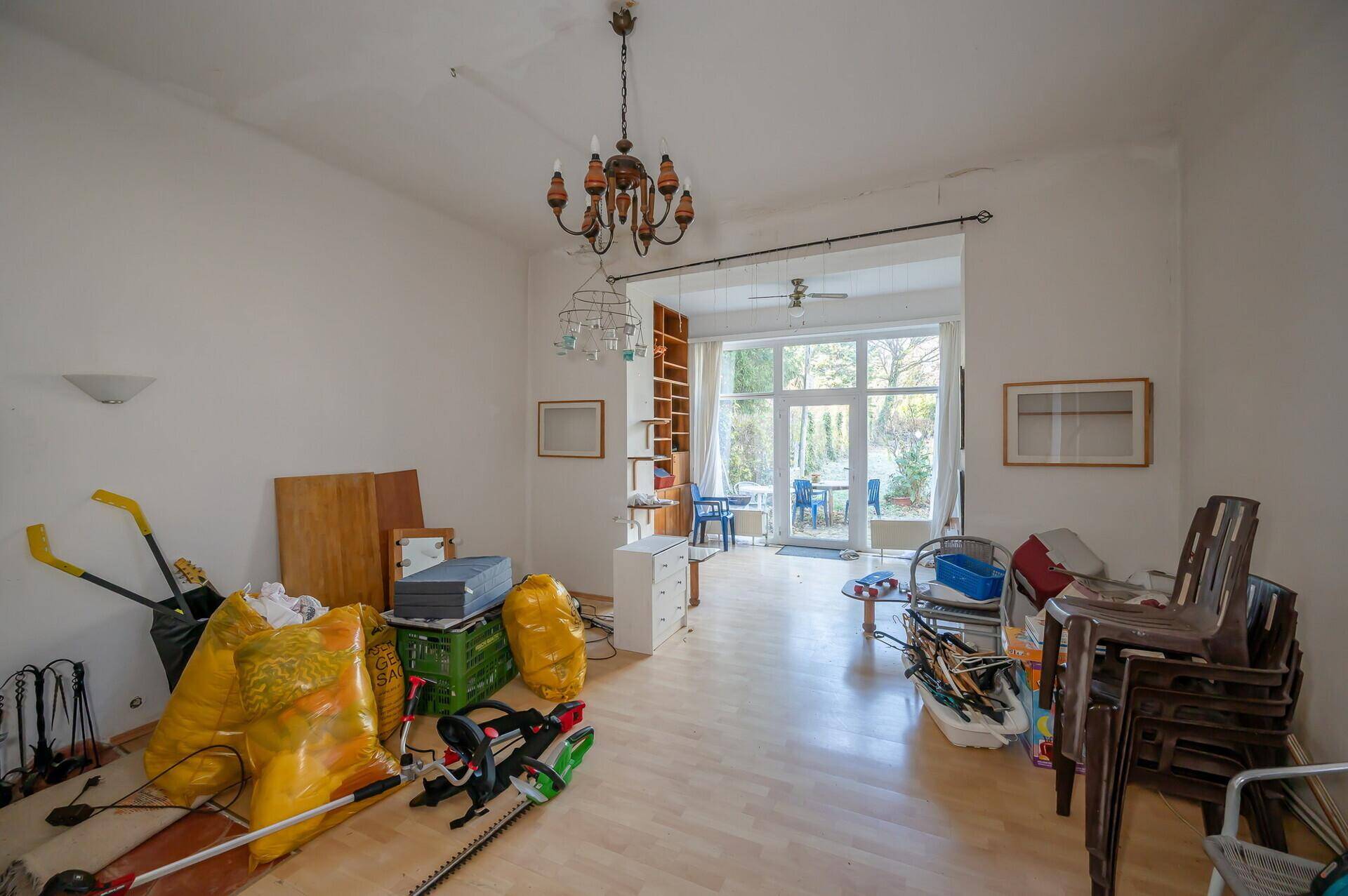 Geräumiges Wohnzimmer mit Parkettboden, Kronleuchter und Blick in den Garten, renovierungsbedürftig.