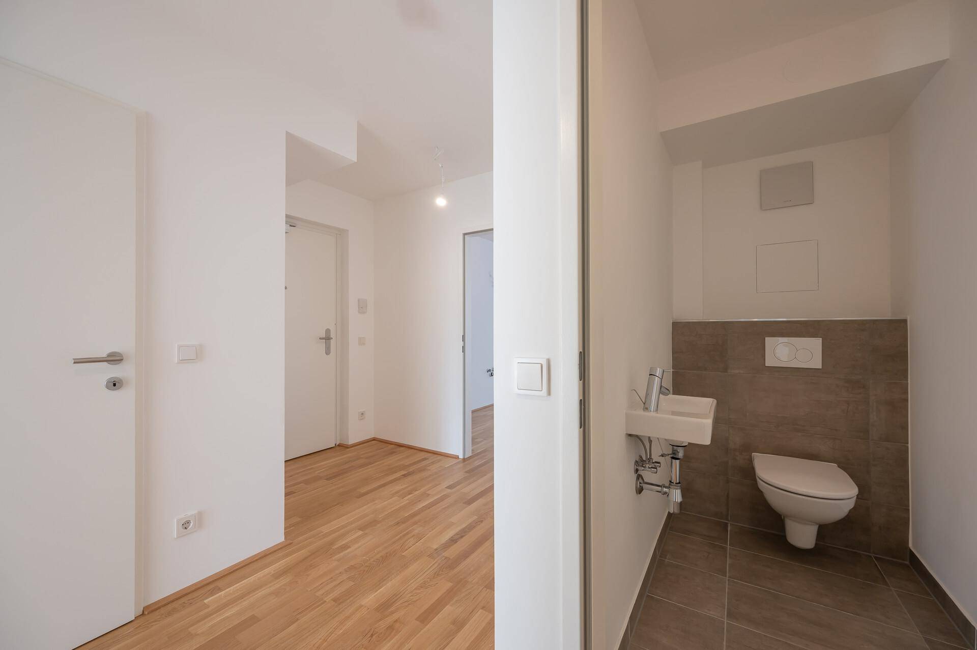 Heller Flur mit Holzboden und Zugang zu einem modernen Gäste-WC mit kleinem Waschbecken.