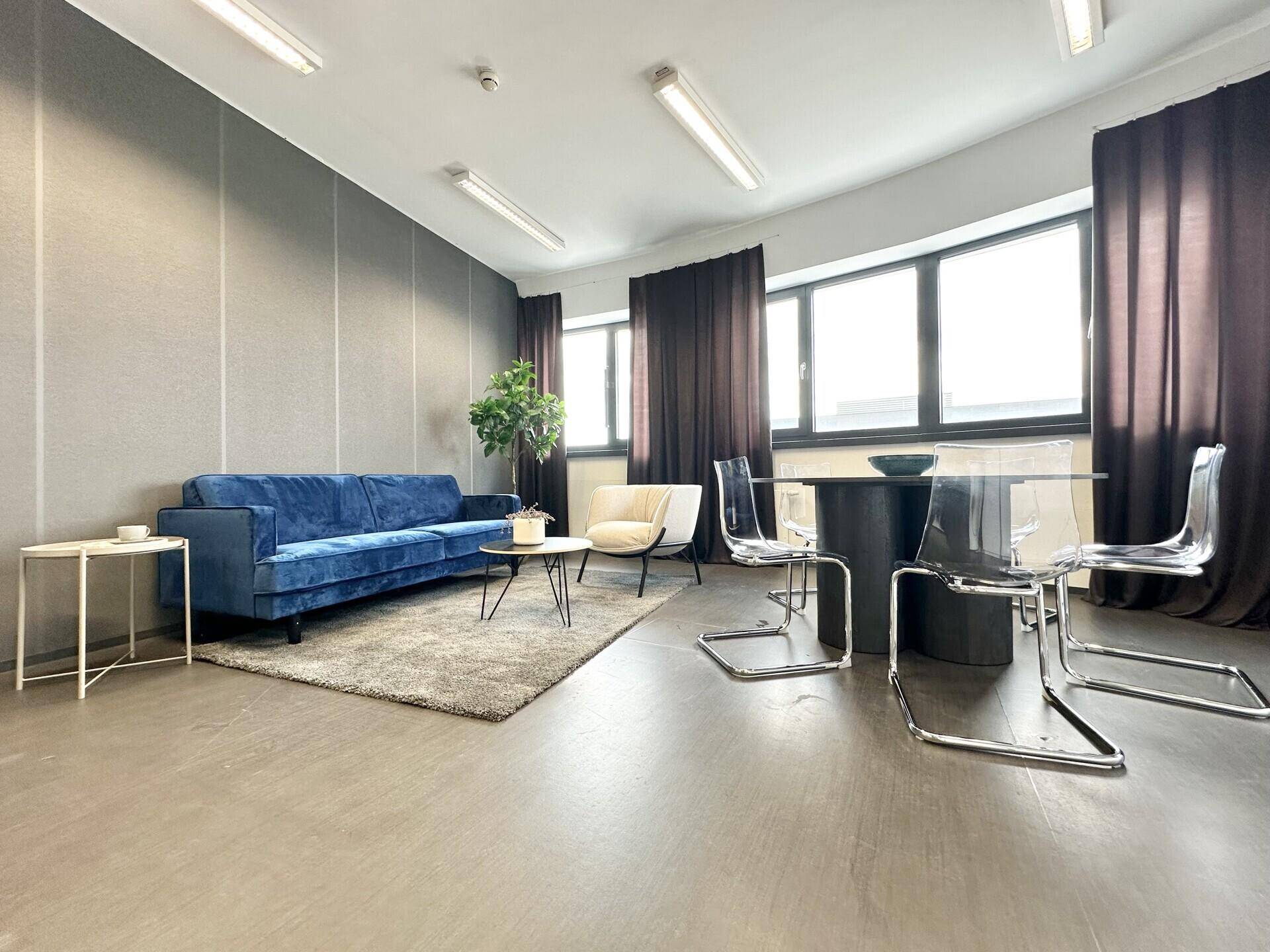 Geräumiger Bürobereich mit blauer Couch, Esstisch und Küchenzeile, ideal für Pausen und Besprechungen.