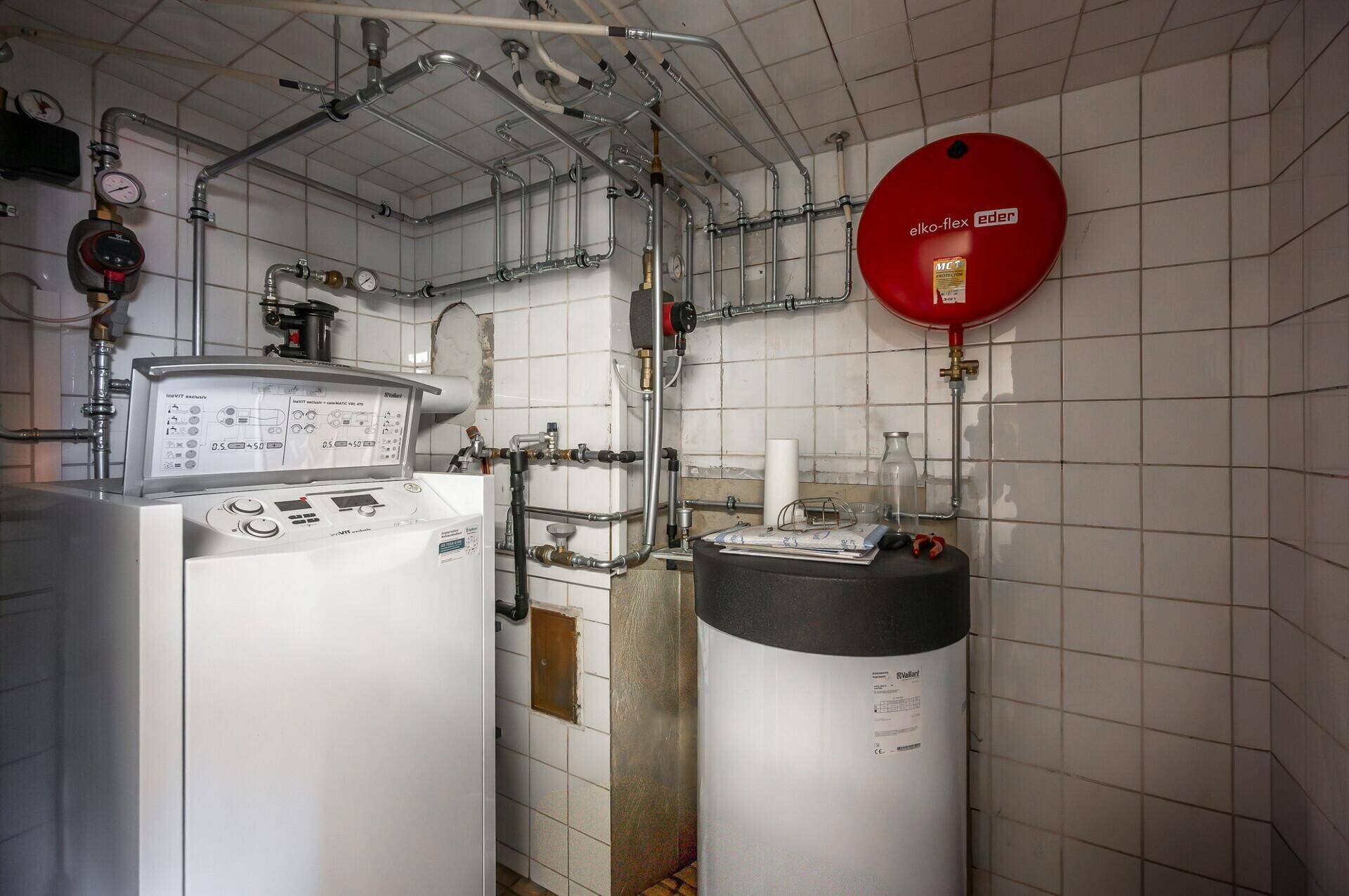 Technikraum mit Heizungsanlage, Warmwasserspeicher und Waschmaschine, gefliesten Wänden.